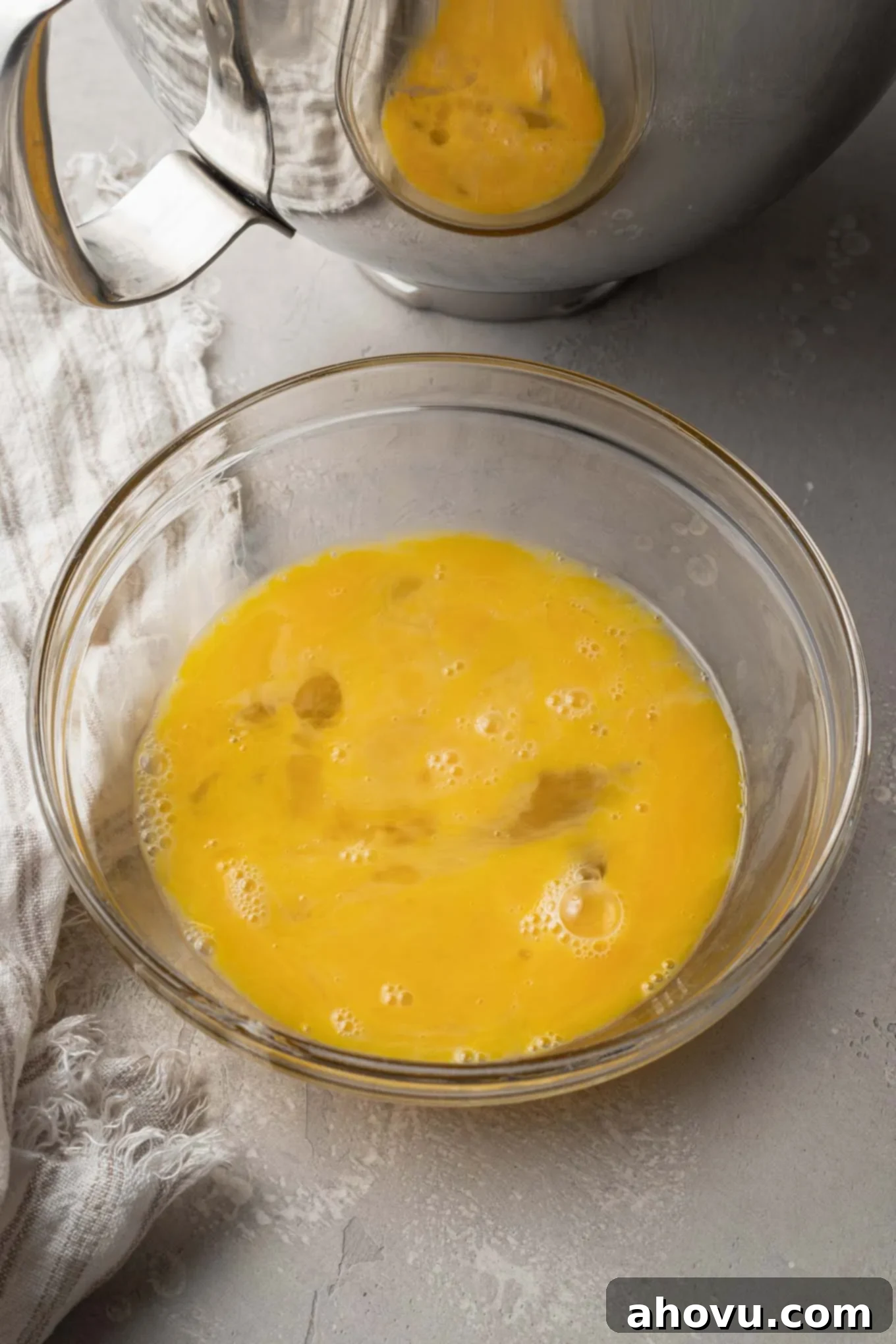 An overhead view of beaten eggs in a glass mixing bowl. 