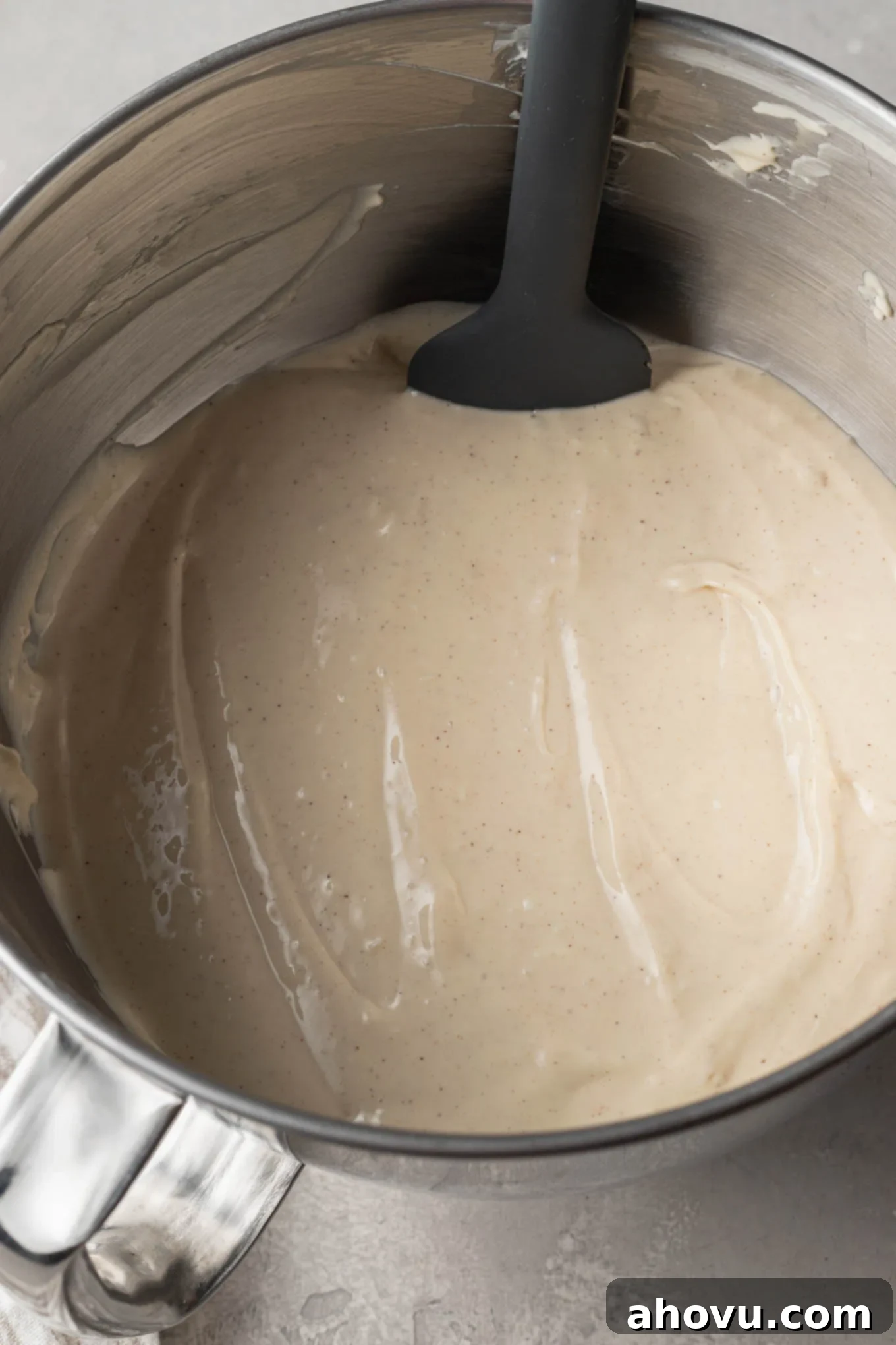 An overhead view of cheesecake filling in the bowl of a stand mixer, with a rubber spatula. 