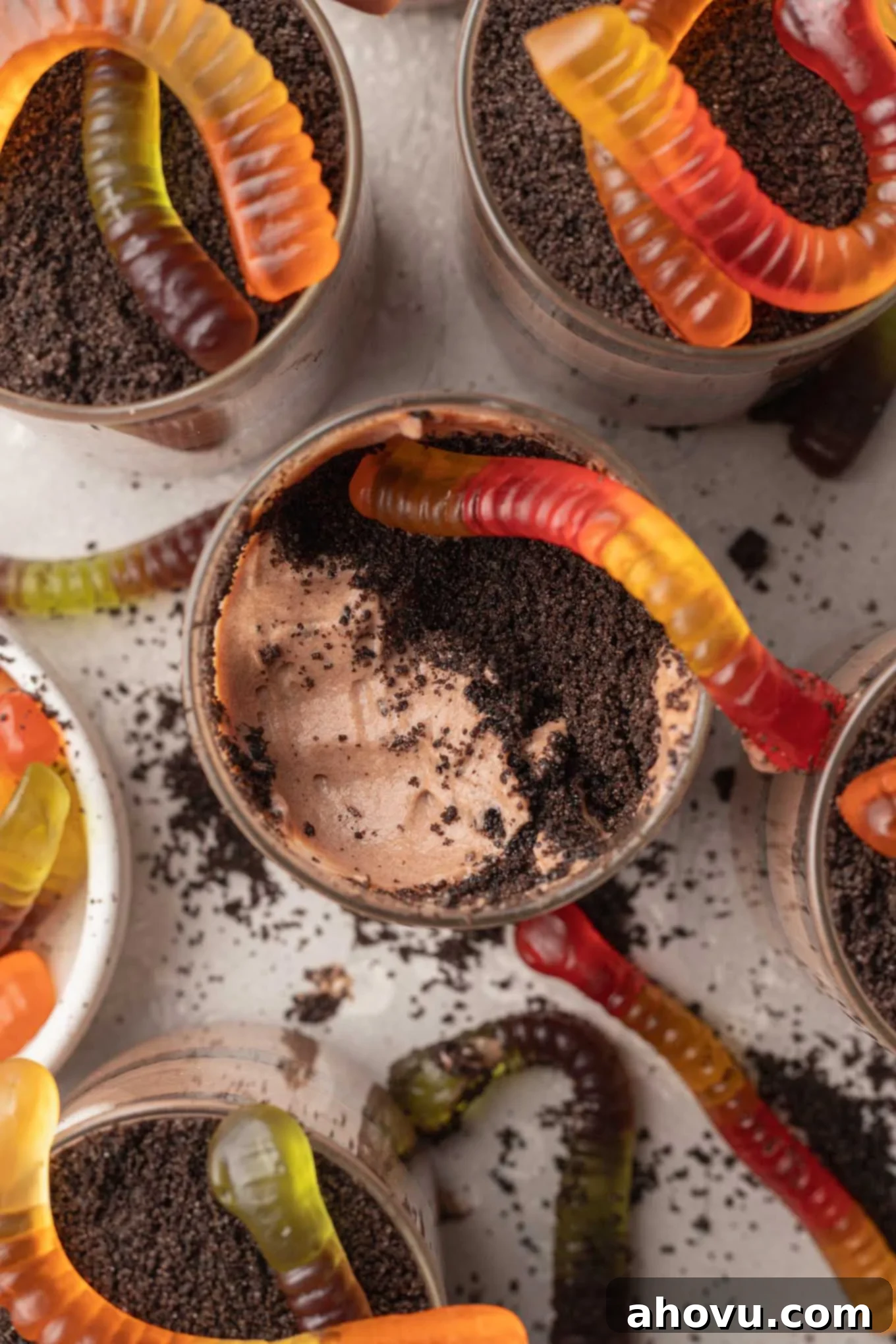 An overhead view of several perfectly assembled Oreo dirt pudding cups, each adorned with gummy worms.
