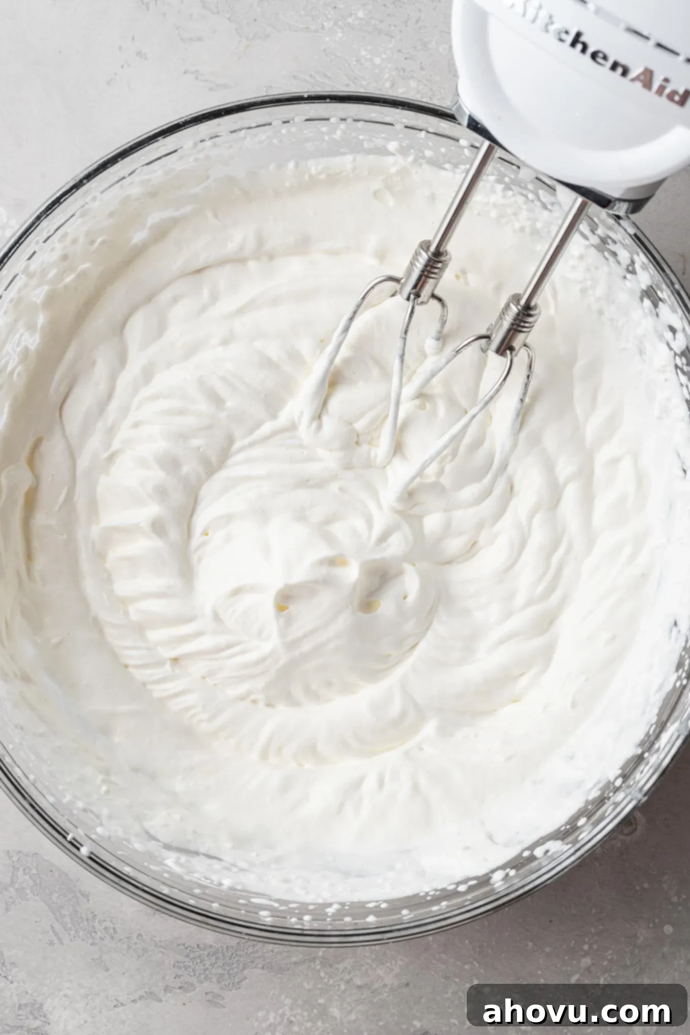 An overhead view of perfectly whipped heavy cream, showcasing stiff peaks in a glass mixing bowl.