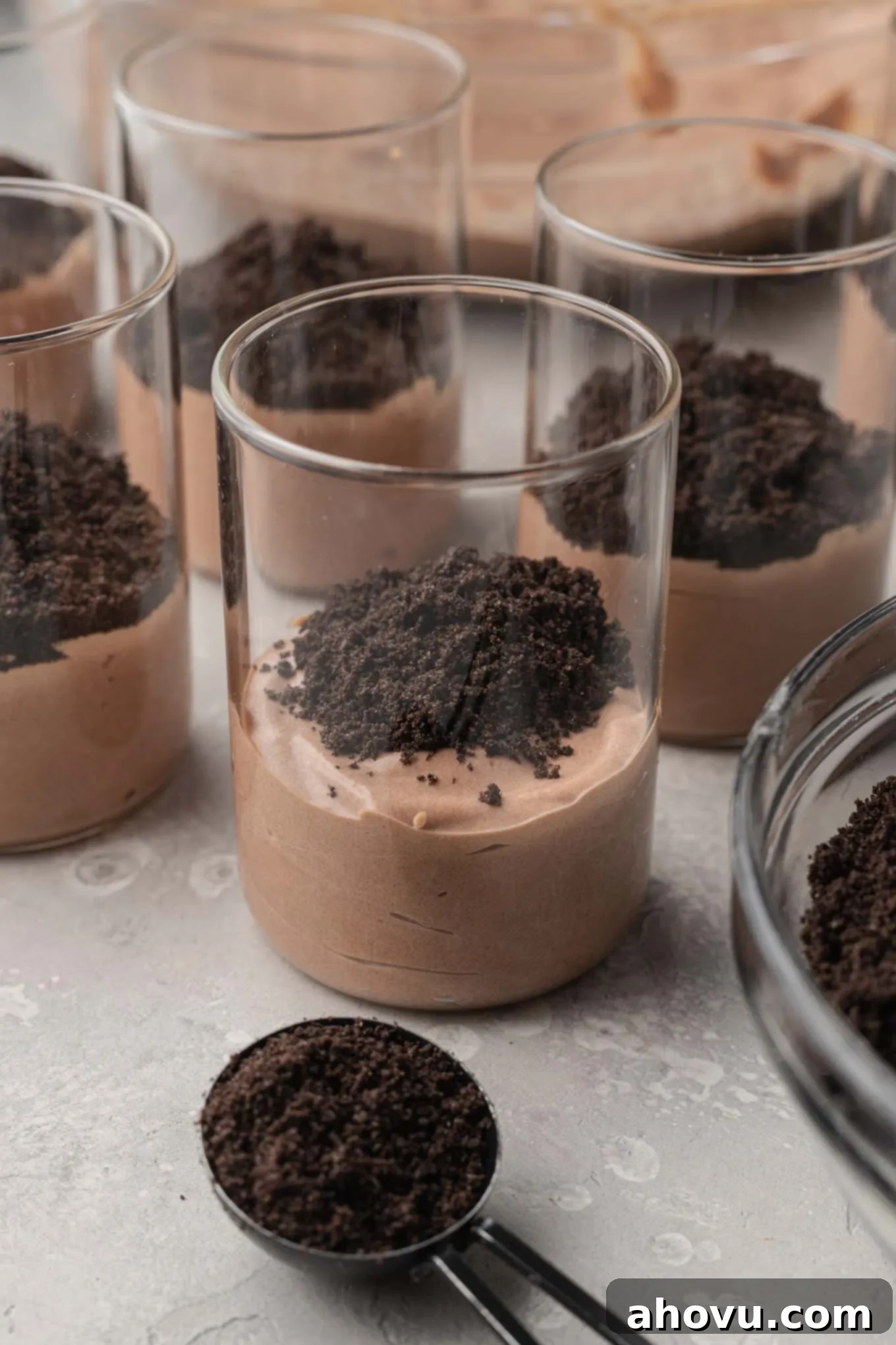 A process shot showing the halfway stage of assembling homemade dirt pudding cups, with layers of pudding and Oreo crumbs.