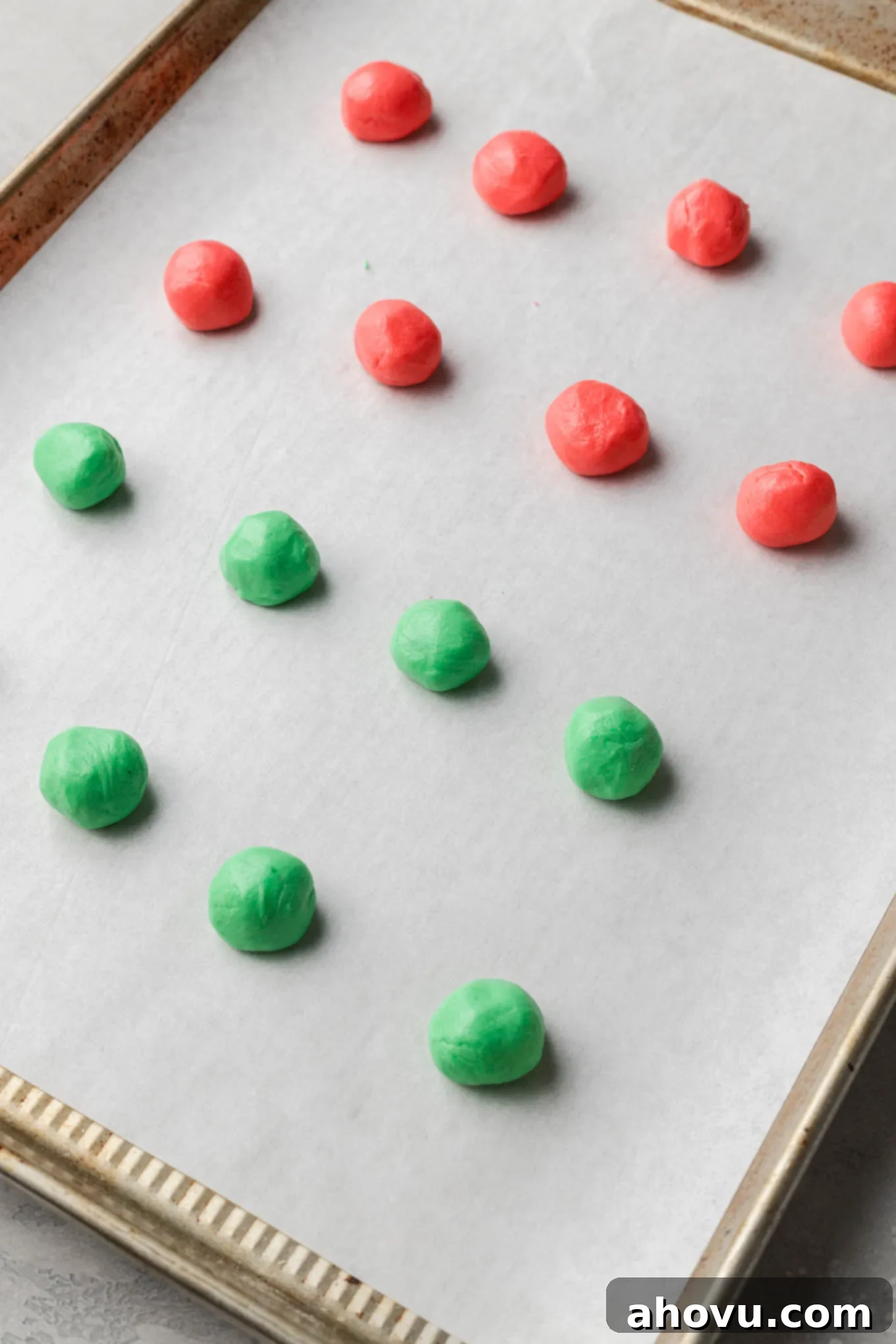 Creamy Dream Mints 8 Red and green balls of Christmas cream cheese mint mixture shaped and placed on a parchment paper-lined baking sheet, ready for indentation.