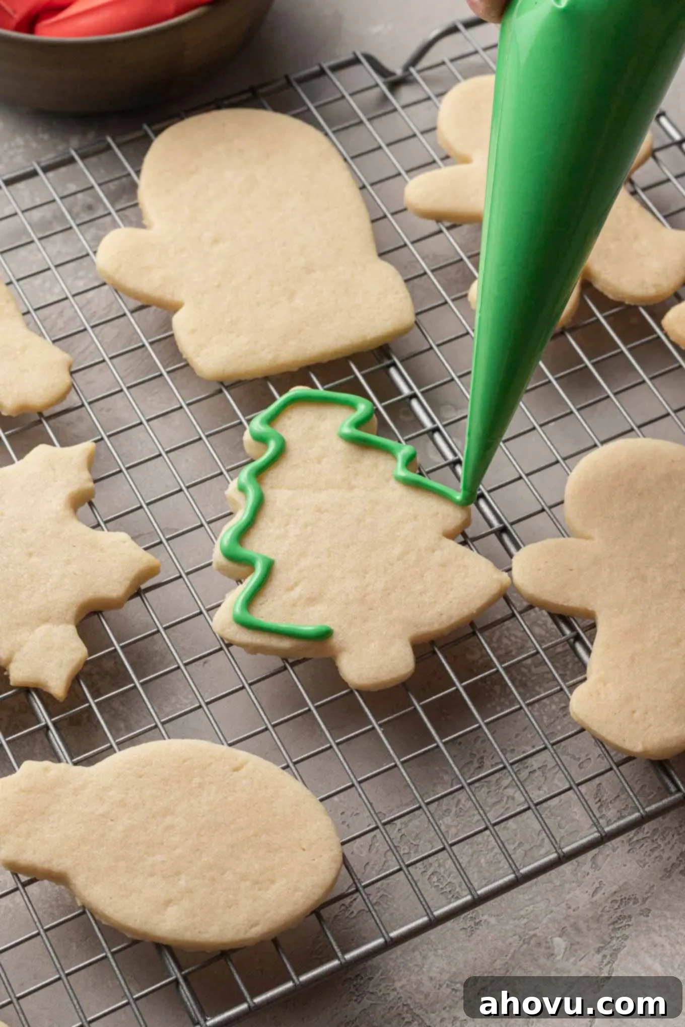 A tree-shaped sugar cookie being meticulously outlined with vibrant green royal icing, forming a crisp barrier for future flooding.