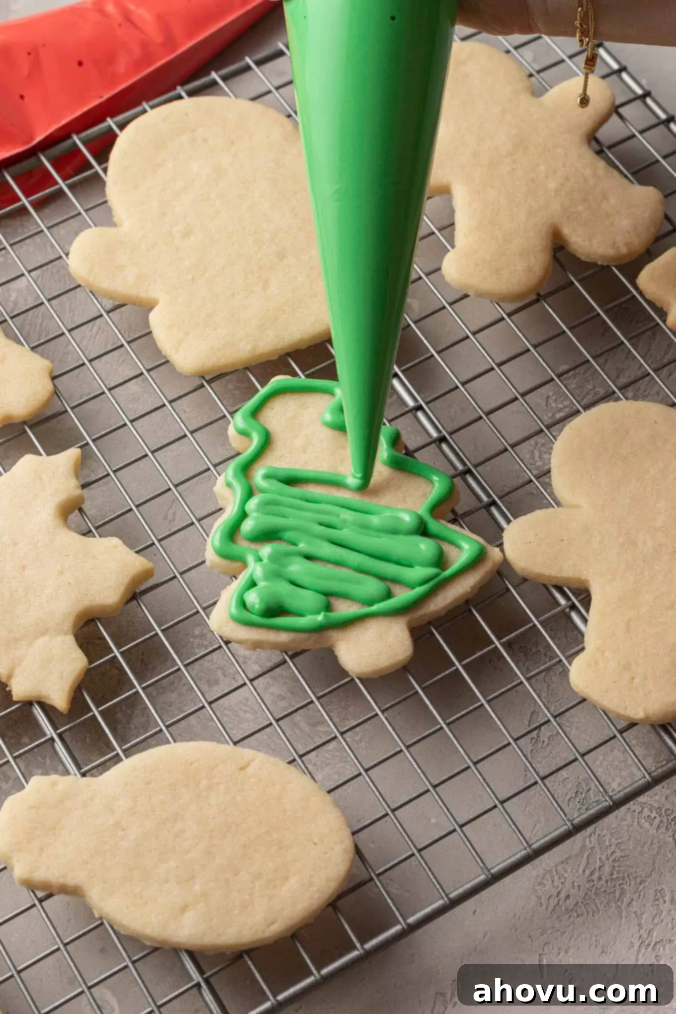 A sugar cookie shaped like a Christmas tree, perfectly outlined and now being meticulously filled with smooth green royal icing for a vibrant base.
