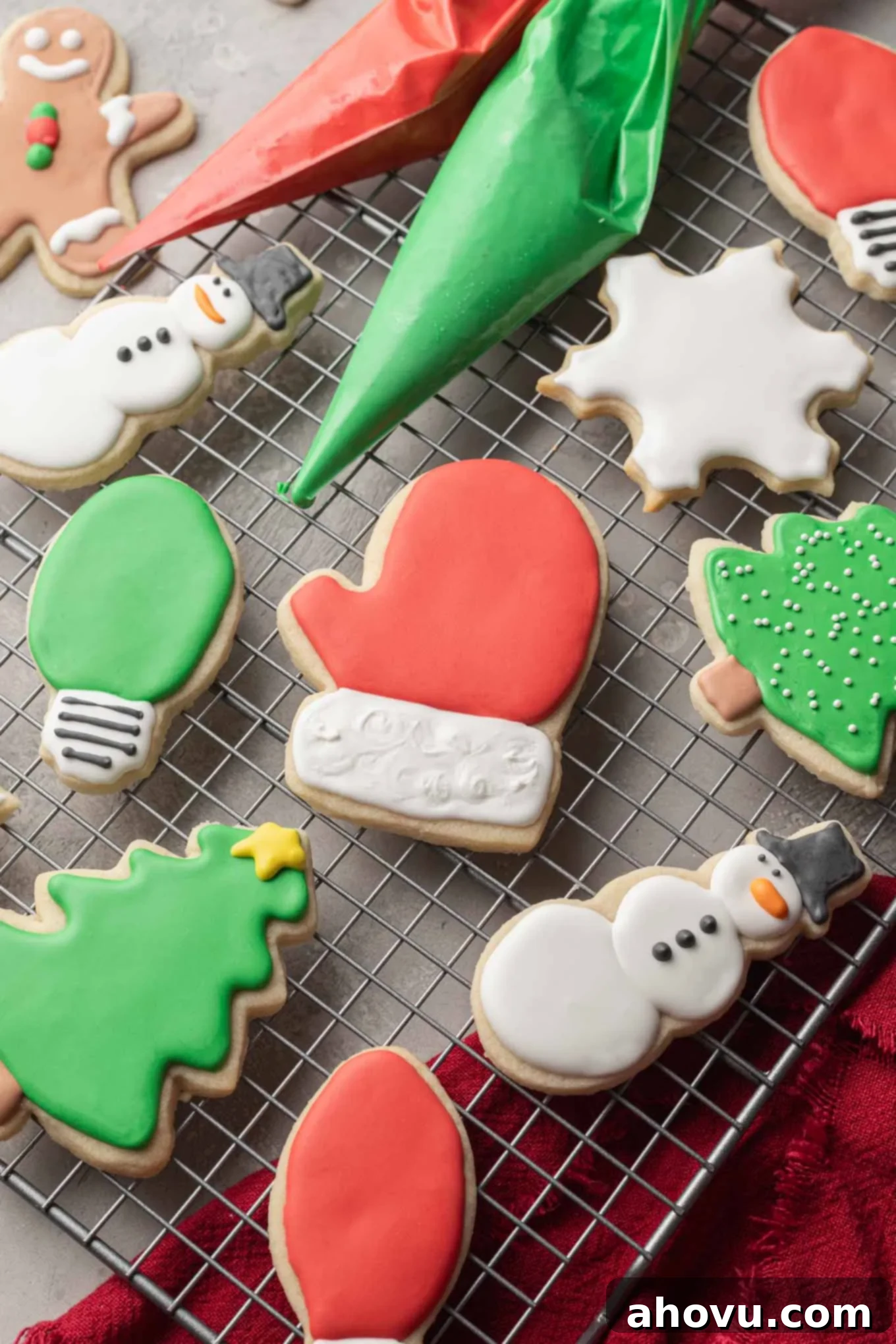 A festive assortment of Christmas-themed sugar cookies, adorned with colorful royal icing, carefully arranged on a wire cooling rack alongside piping bags filled with red and green icing.