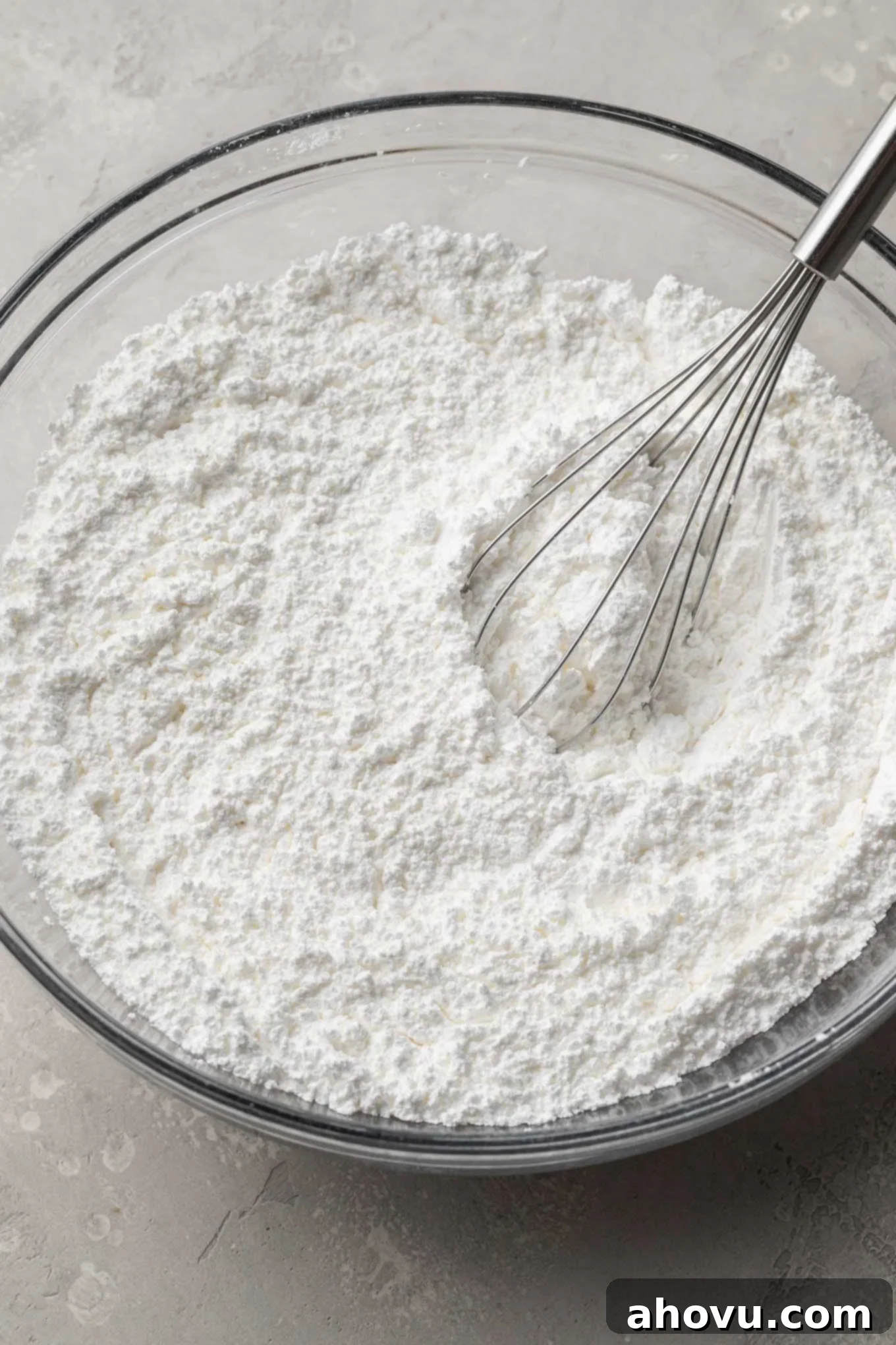 Close-up view of meringue powder and powdered sugar perfectly whisked together in a clear glass mixing bowl, ready for the next step in royal icing preparation.