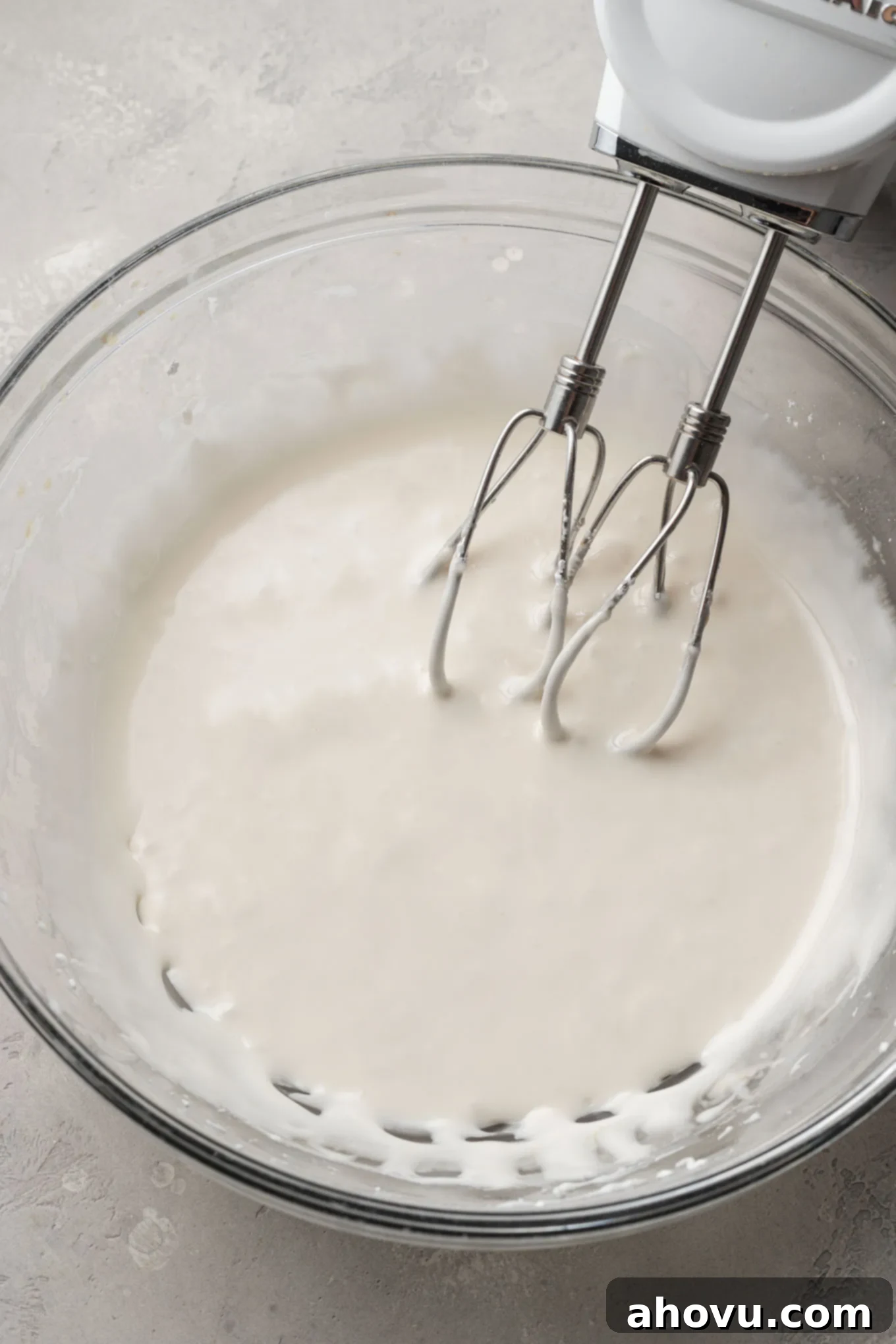 Warm water, a touch of corn syrup, and aromatic vanilla extract being carefully added to the mixing bowl, blending with the dry royal icing ingredients.