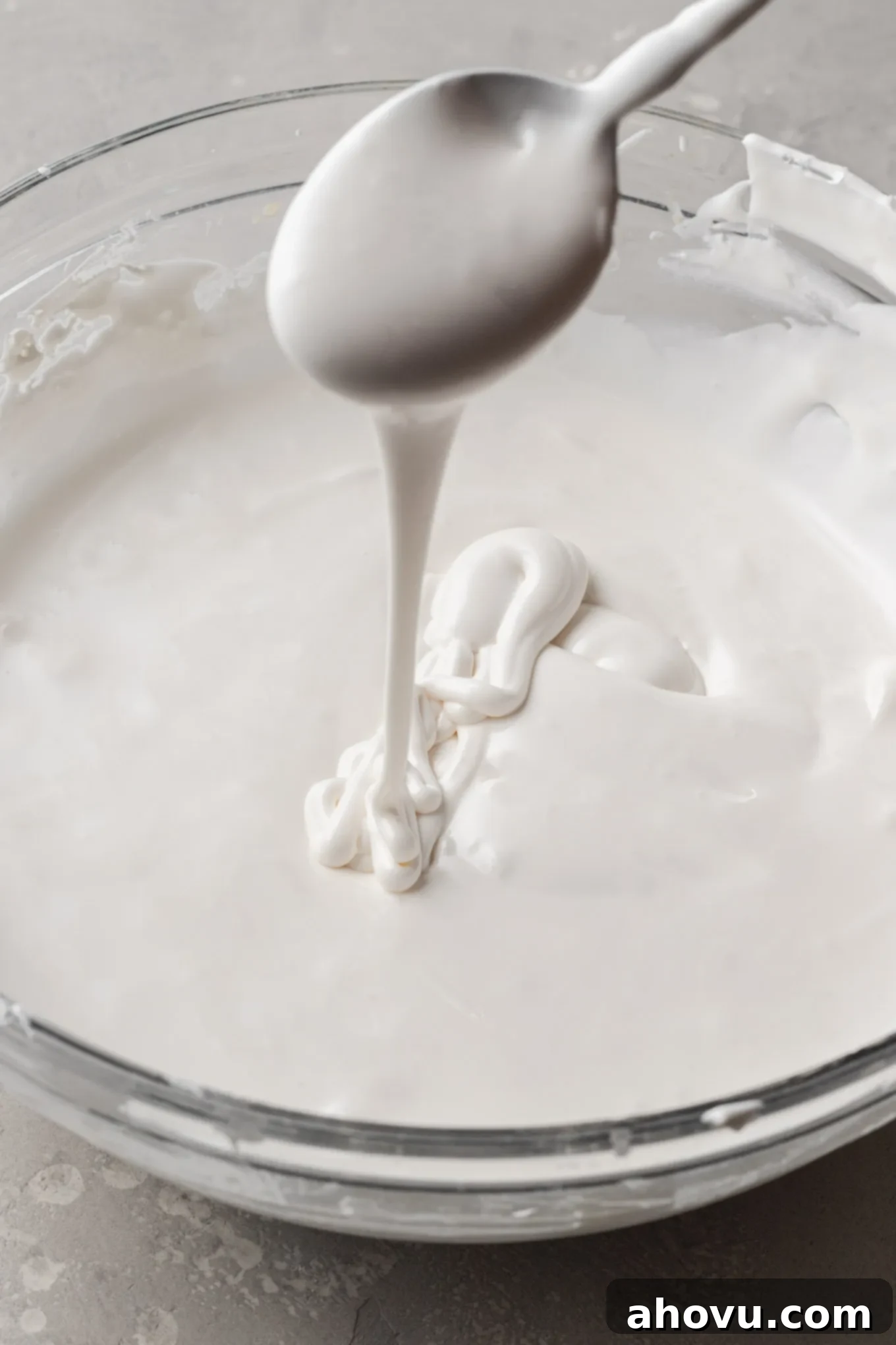 Royal icing thinned to a versatile medium consistency, with a spoon demonstrating the 15-second flow rate back into the bowl.