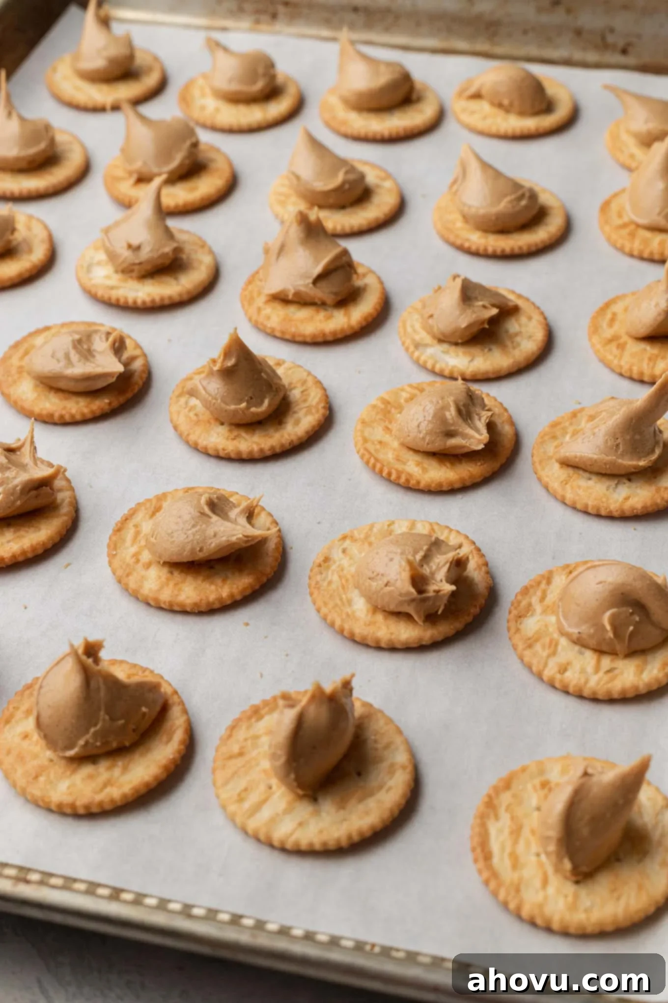 Rows of crackers dolloped with peanut butter filling, lined up on a baking sheet. 