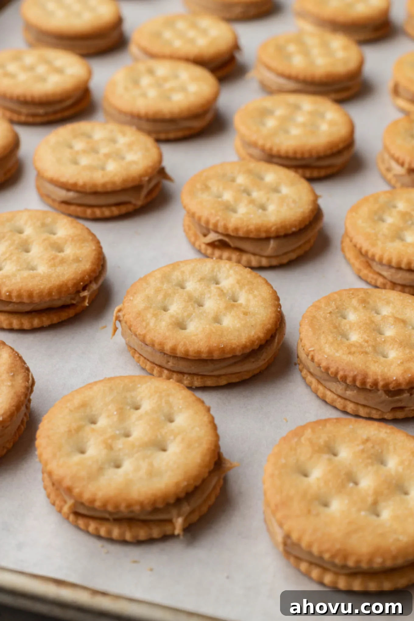 Rows of crackers filled with peanut butter, on a baking sheet. 