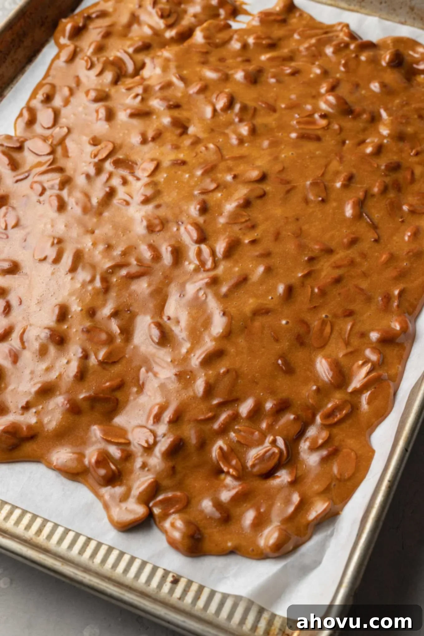 Golden Peanut Brittle 7 An overhead view of hot peanut brittle spread over a parchment paper-lined cookie sheet to cool.
