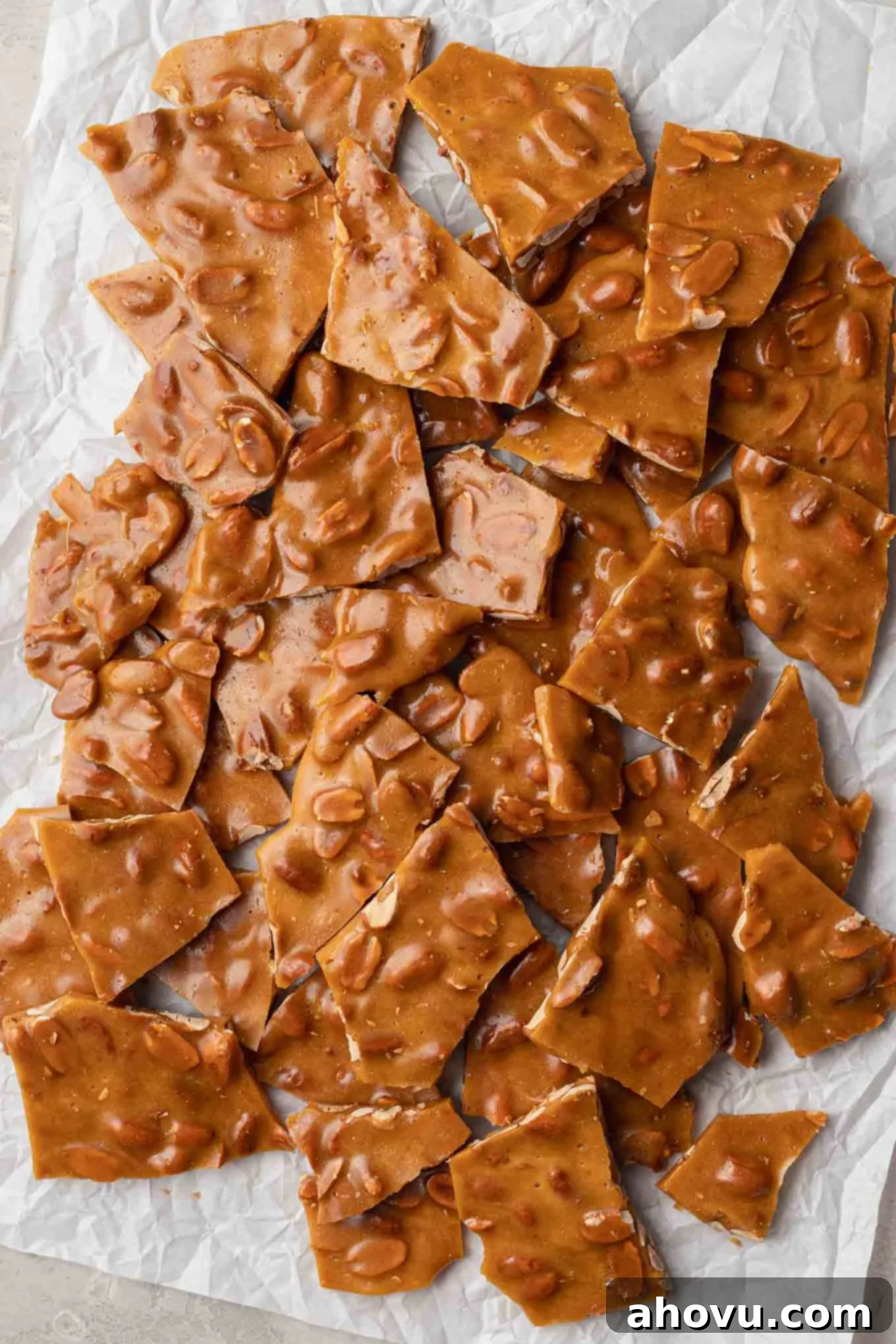 Golden Peanut Brittle 8 An overhead view of homemade peanut brittle, broken into pieces on parchment paper.
