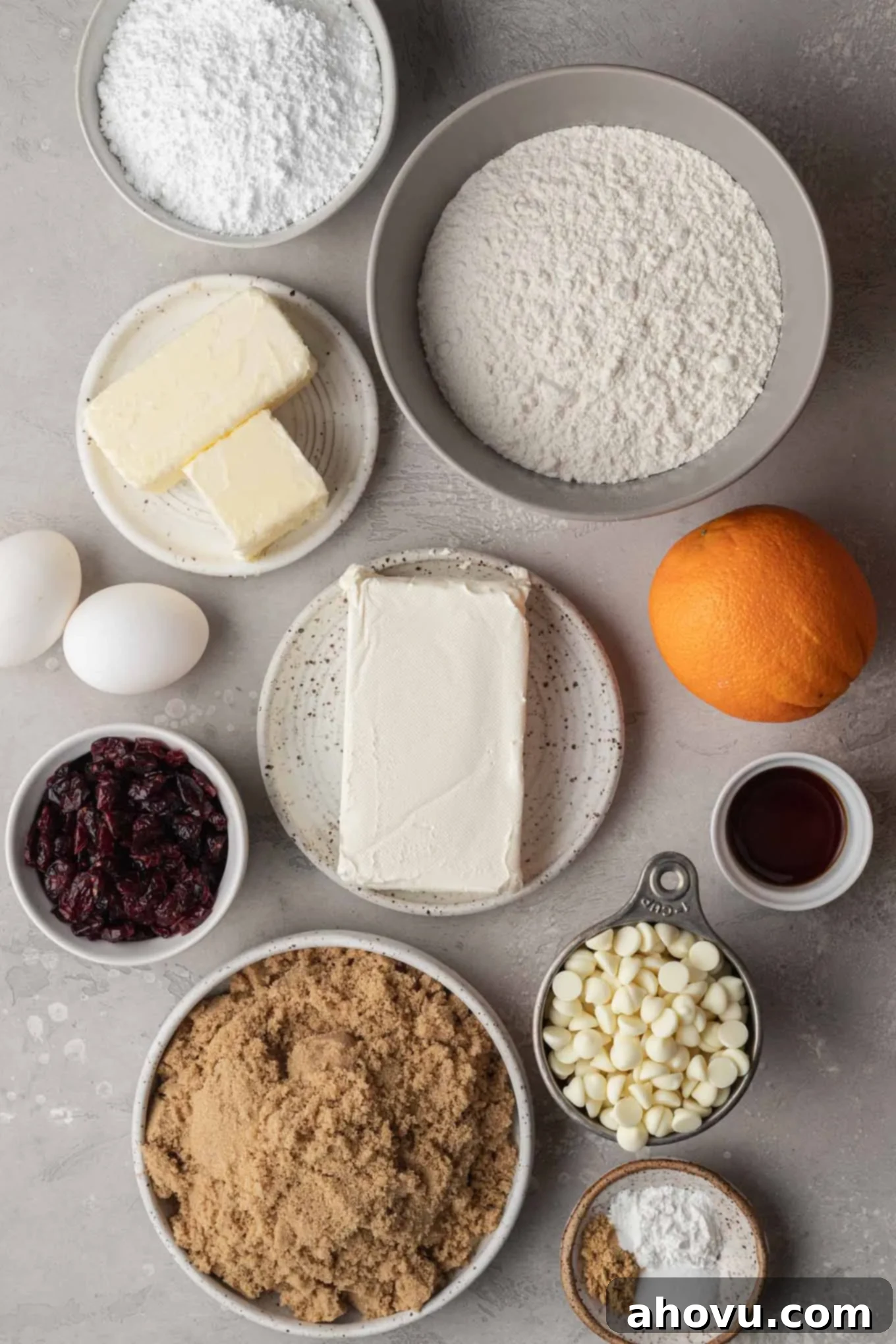 An overhead view of all the fresh, high-quality ingredients laid out on a clean surface, ready to be used to make homemade cranberry bliss bars, including butter, sugar, flour, eggs, cranberries, and white chocolate.