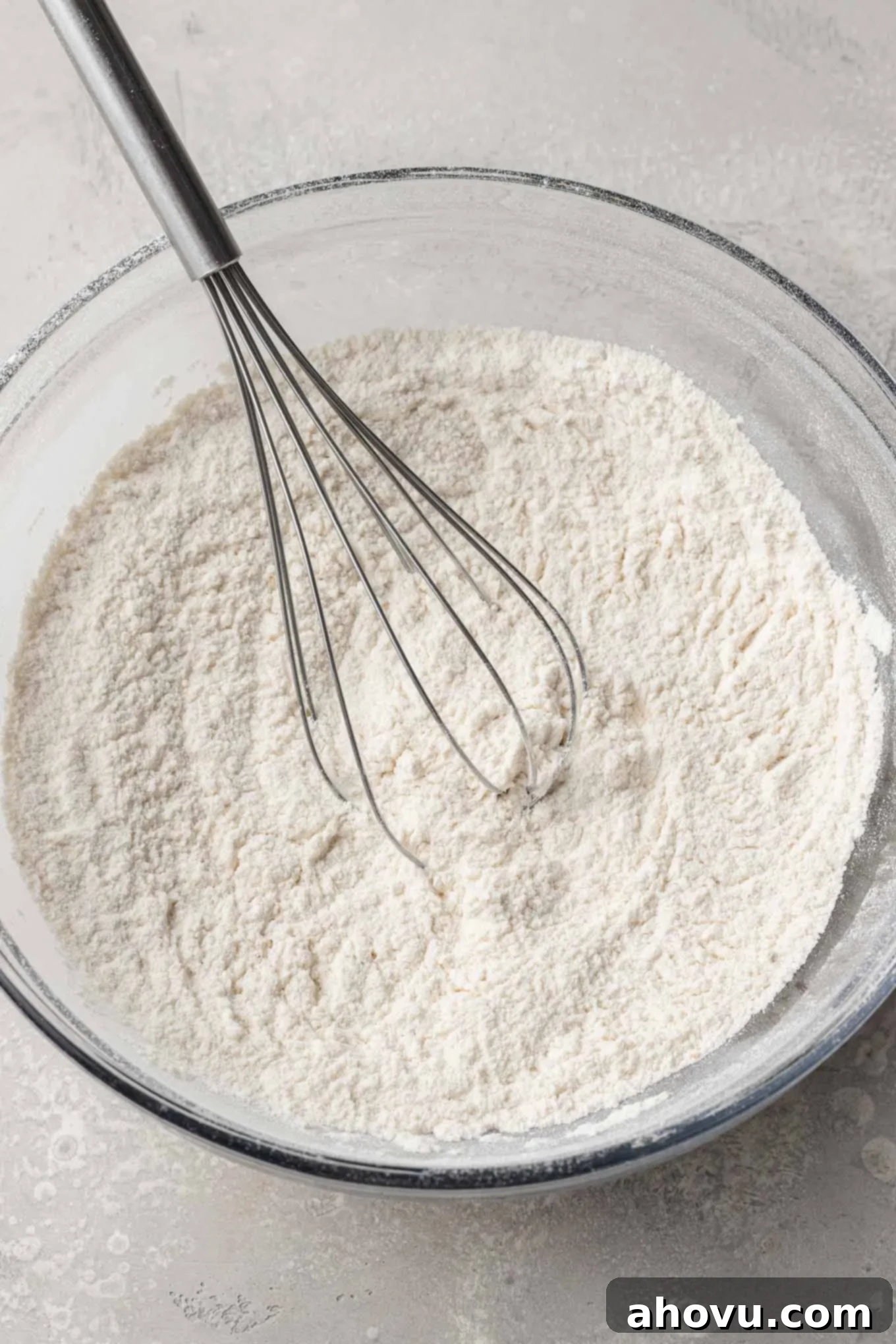 An overhead view of all-purpose flour, baking powder, ground ginger, and salt combined in a glass mixing bowl, perfectly measured and ready for the next step in making cranberry bliss bars.