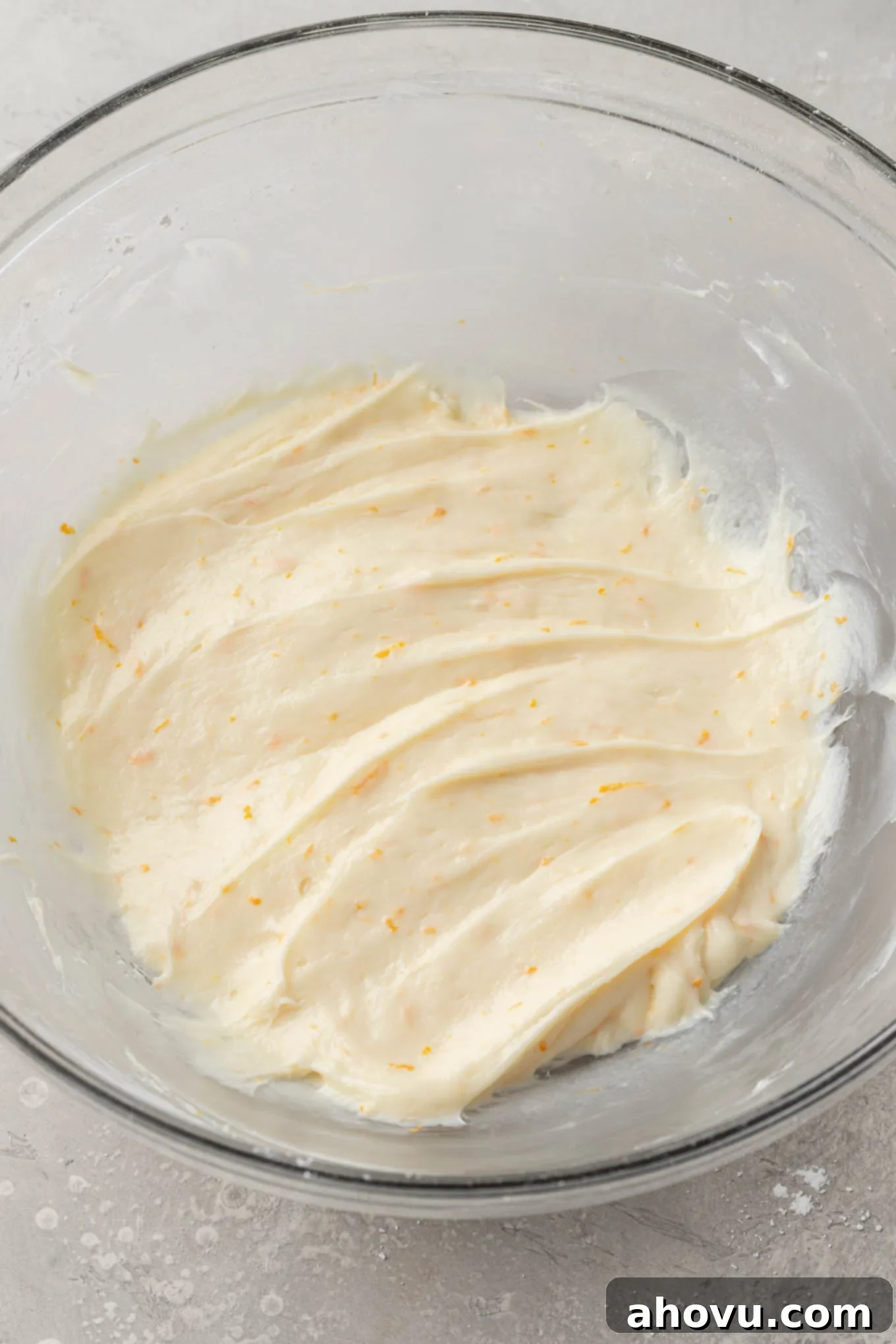 An overhead view of the completed orange cream cheese frosting in a glass mixing bowl, showcasing its smooth, creamy texture and light orange tint, ready to be spread over the cooled blondies.