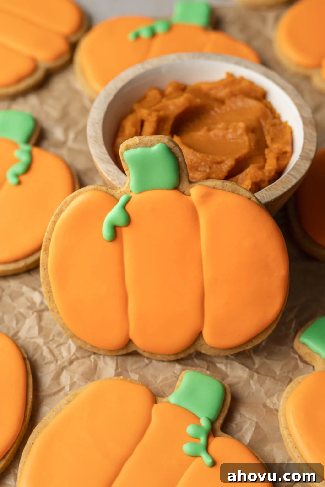 Autumn Pumpkin Sugar Cookies 2 A pumpkin-shaped sugar cookie resting against a small dish of pumpkin puree.
