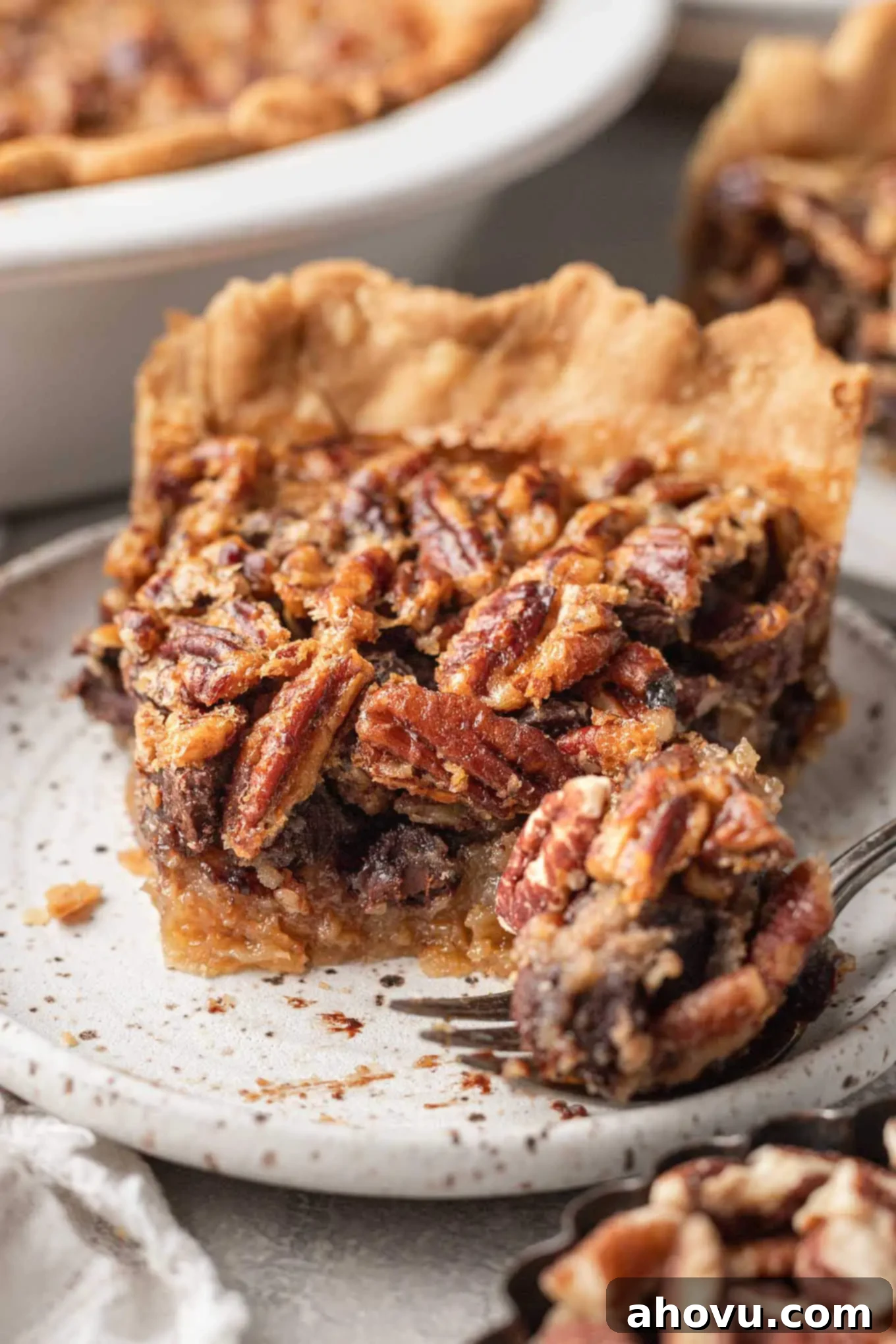 Decadent Chocolate Pecan Dream 13 A charming front view of a single slice of chocolate pecan pie on a speckled dessert plate, with a fork poised for a delicious bite in the foreground.