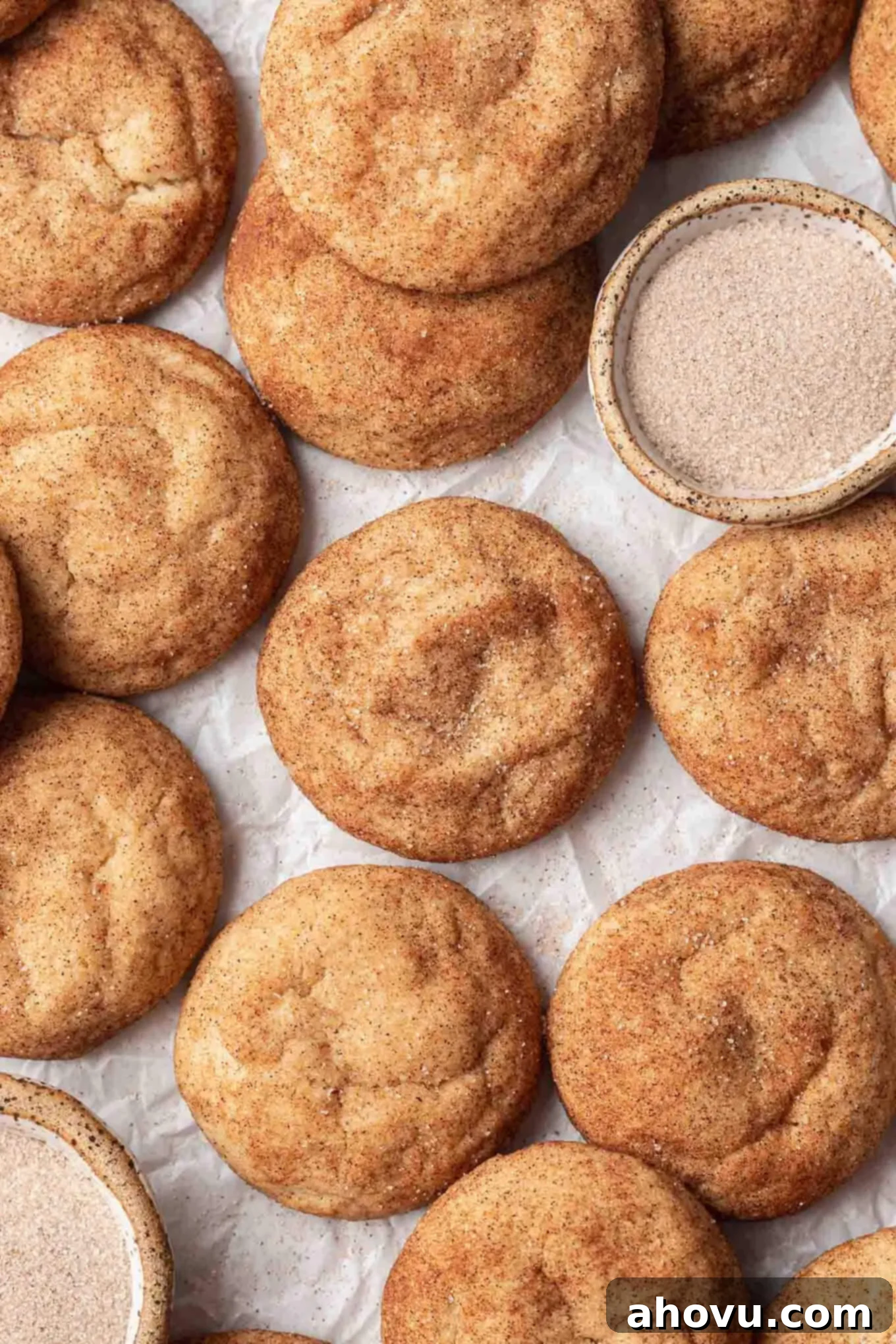 An overhead view of browned butter snickerdoodles on parchment paper, with a dish of cinnamon sugar on the side. 