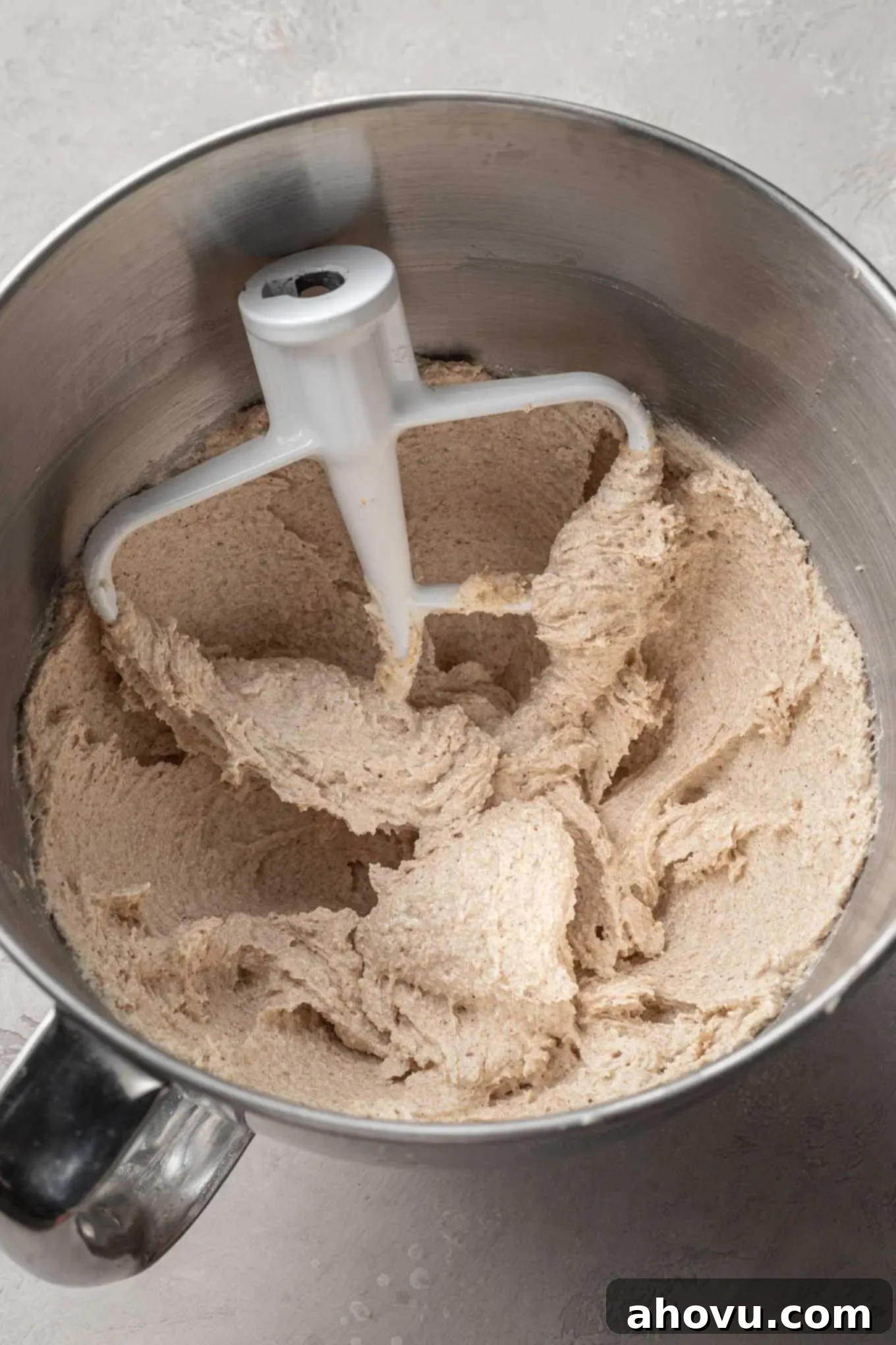 An overhead view of creamed brown butter and sugar in a mixing bowl, with a paddle attachment. 