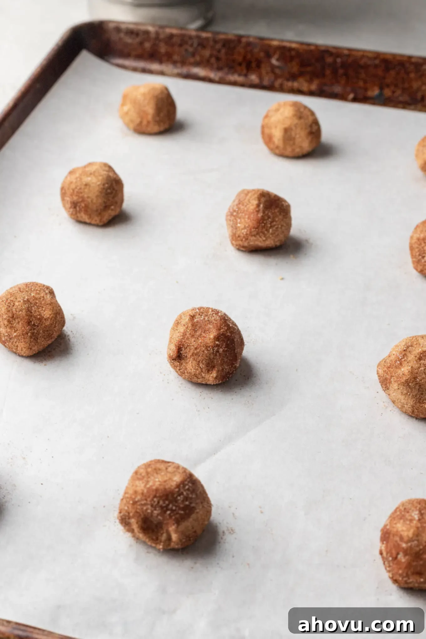 Raw brown butter snickerdoodle cookie dough balls on a parchment paper-lined baking sheet. 