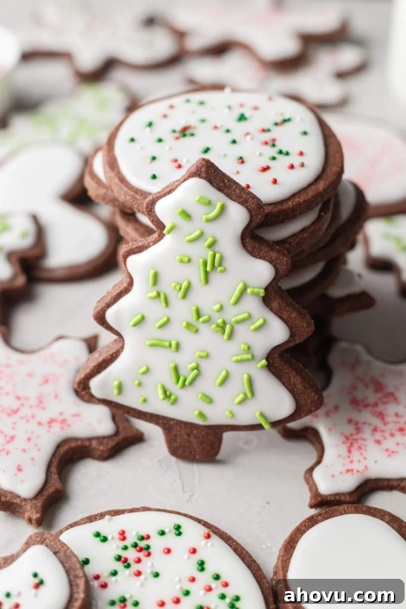 A stack of chocolate sugar cookies, decorated with festive icing and sprinkles. A tree-shaped cookie leans against the stack.