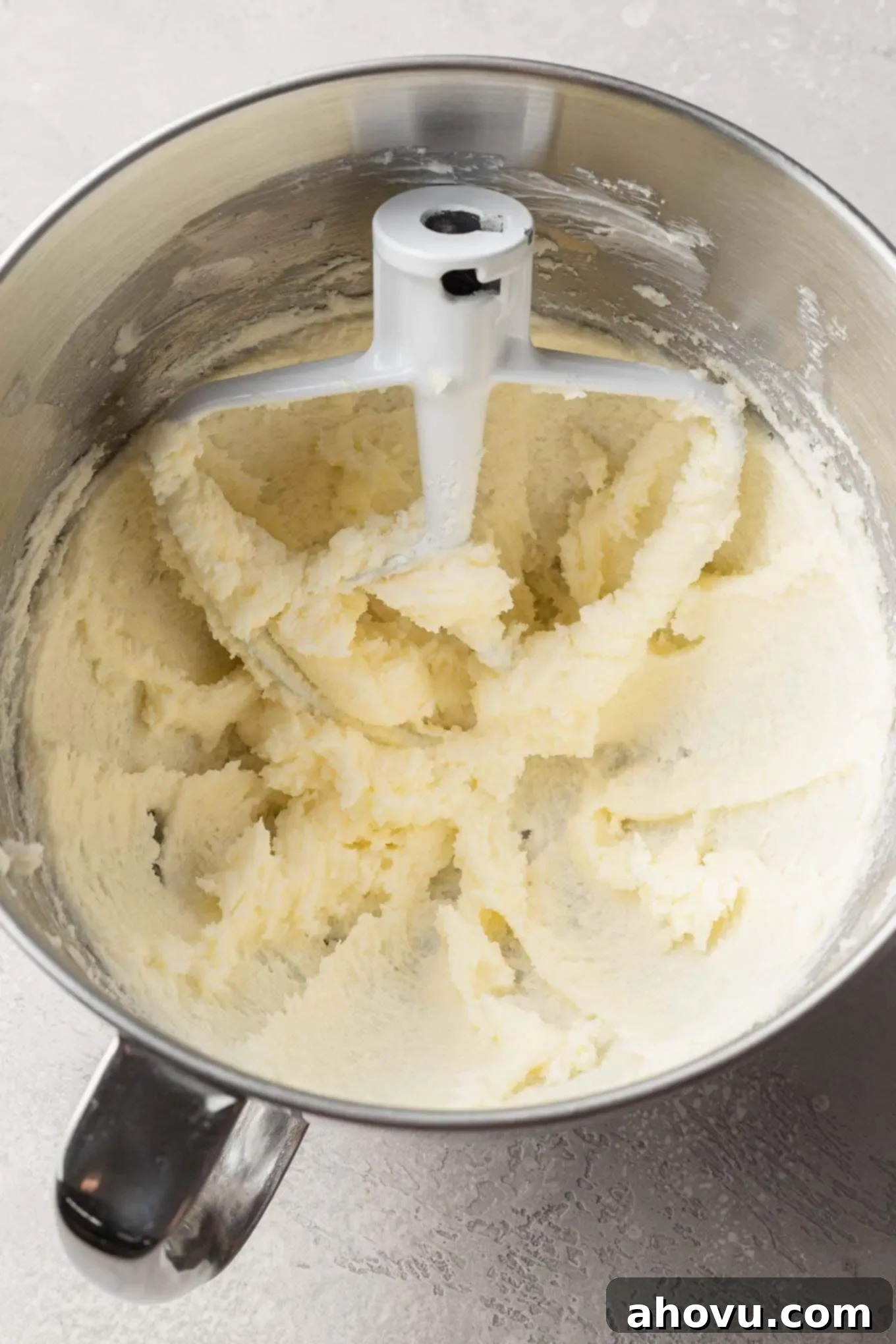 An overhead view of softened butter and granulated sugar creaming together in a stand mixer bowl with a paddle attachment.