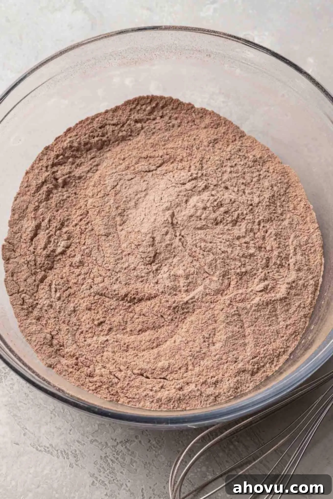 An overhead view of sifted cocoa powder and all-purpose flour in a glass mixing bowl, ready to be combined.