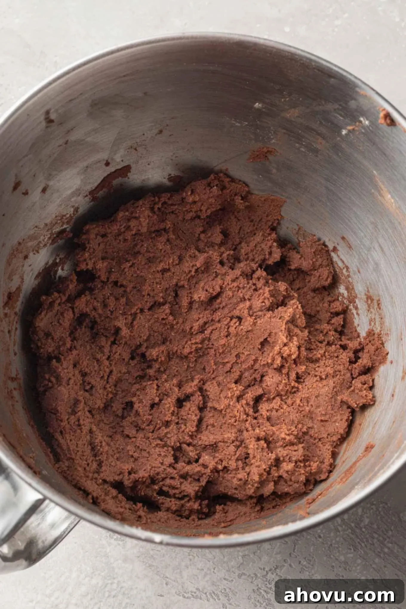 An overhead view of rich cocoa powder sugar cookie dough mixed in a stainless steel mixing bowl.
