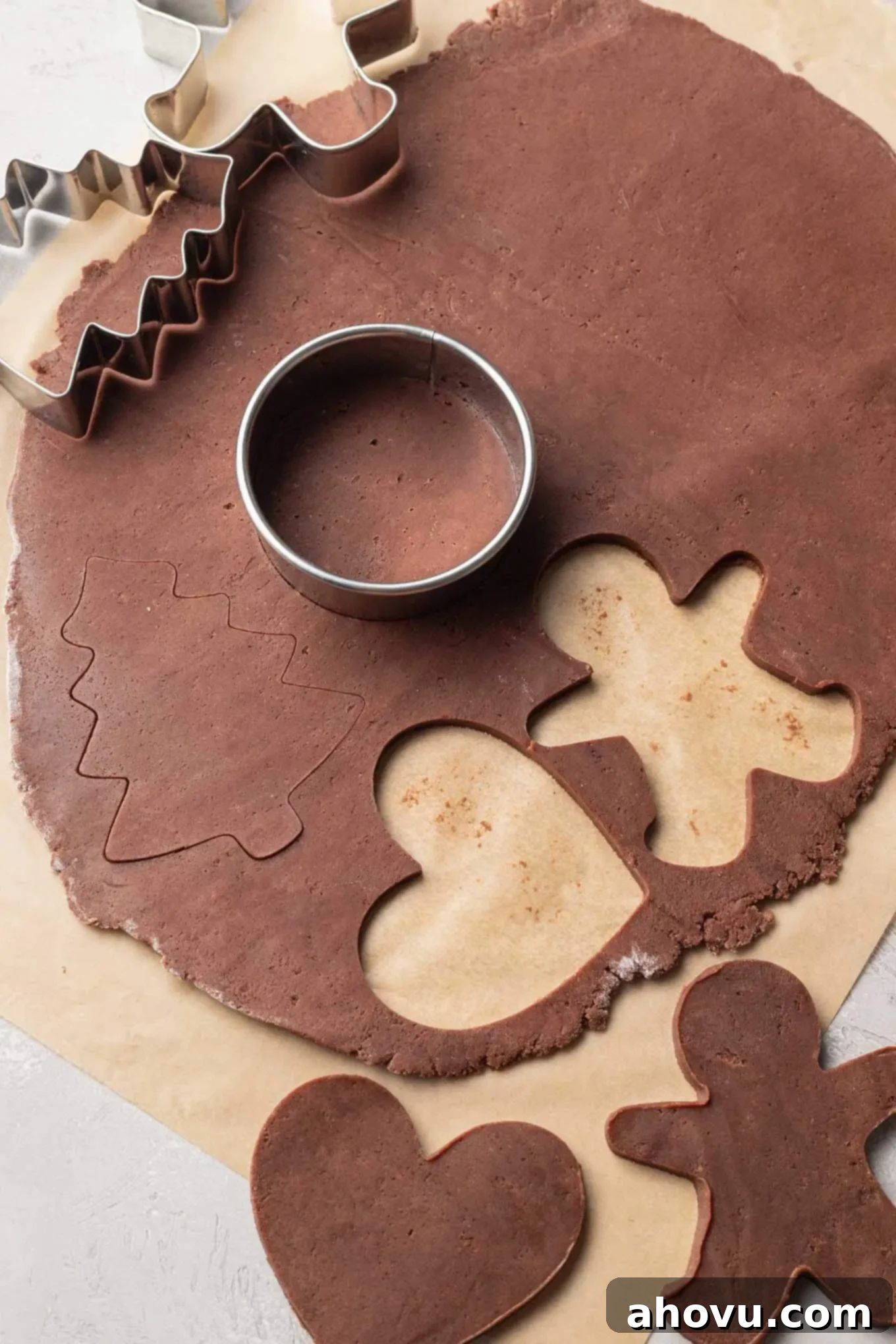An overhead view of chocolate sugar cookie dough being precisely cut into various festive shapes using cookie cutters.
