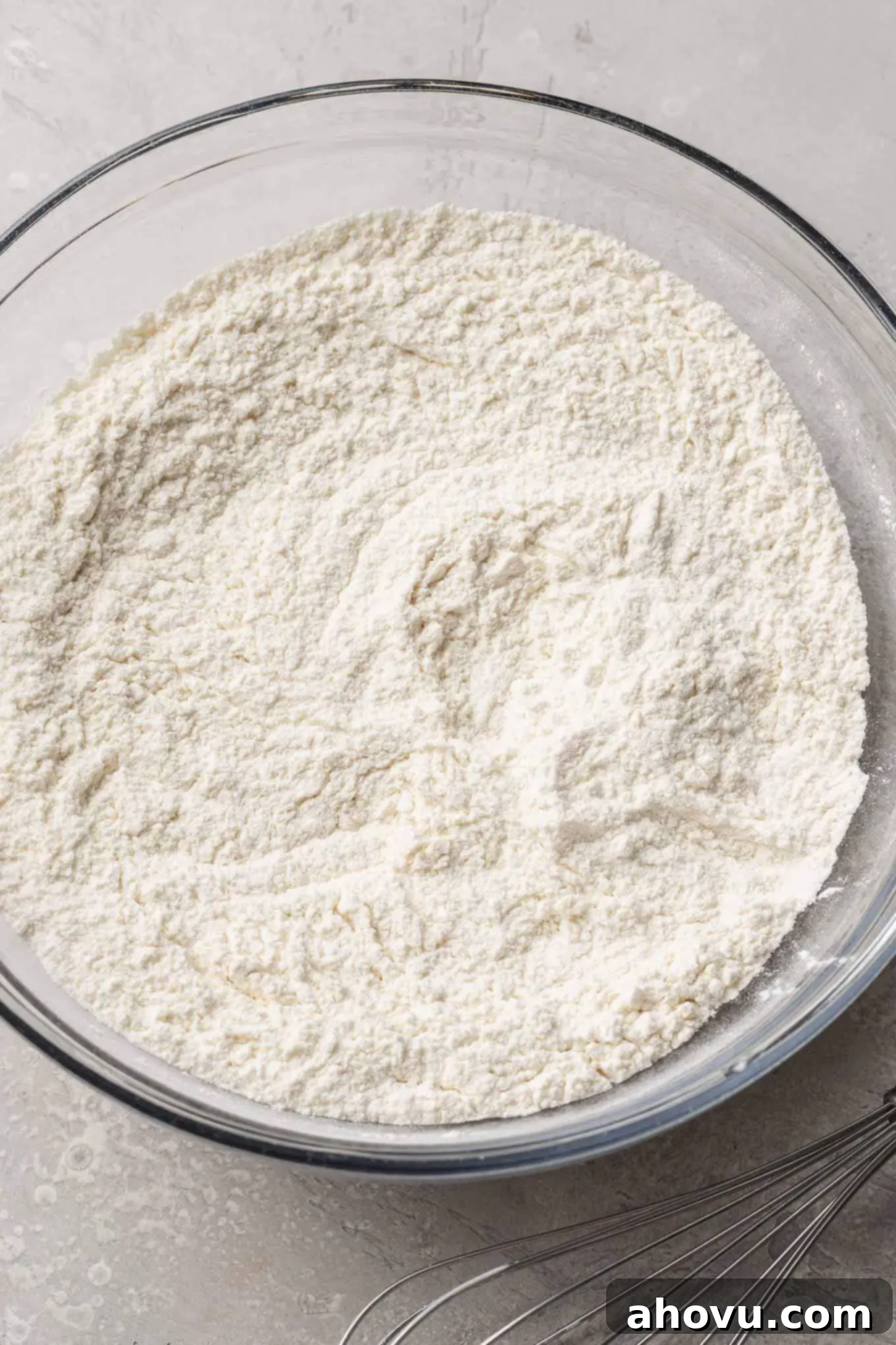 Flour, baking powder, and salt precisely whisked together in a clear glass mixing bowl, ready for cookie dough preparation.