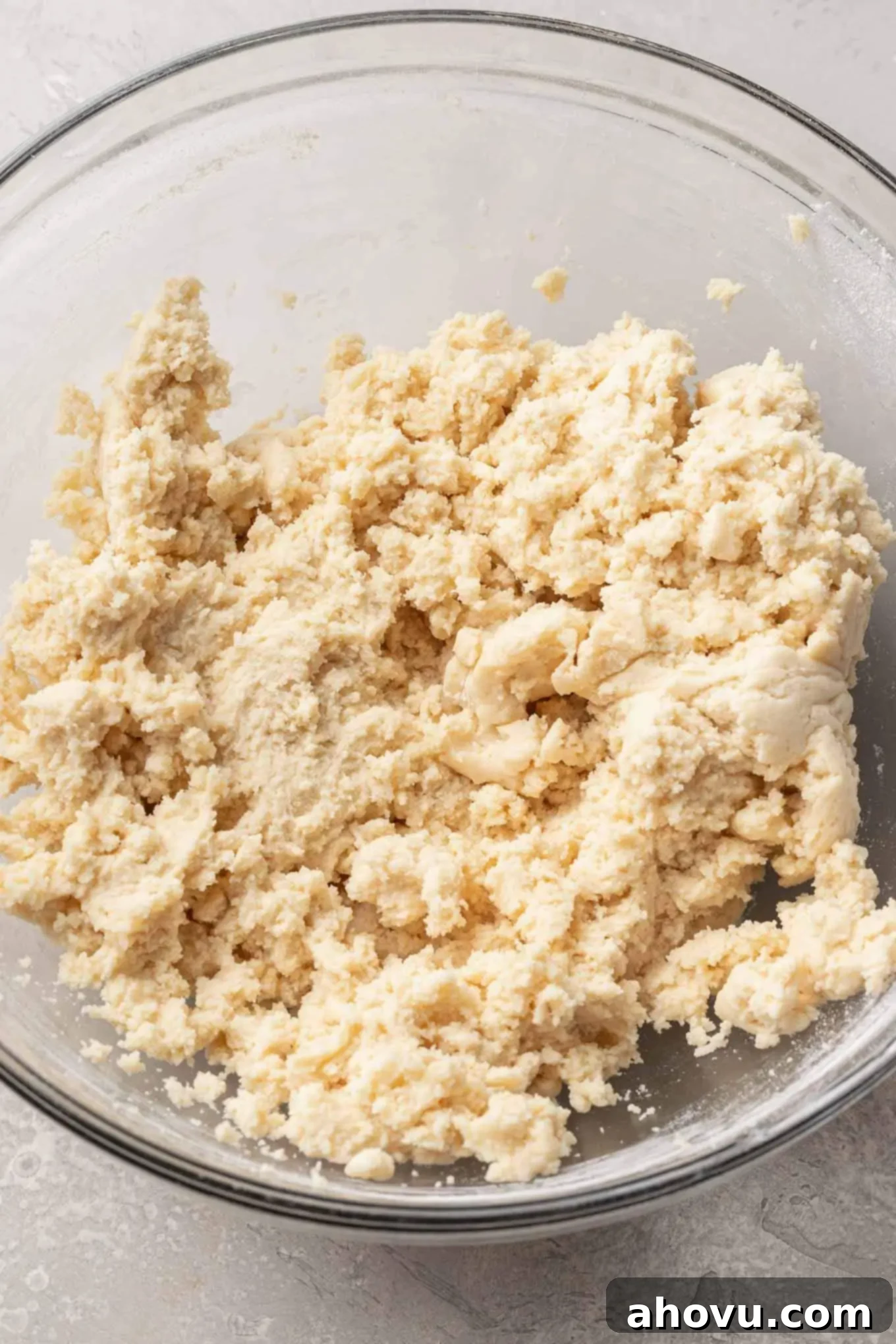 An overhead view of perfectly mixed sugar cookie dough, smooth and ready for rolling, resting in a clear glass mixing bowl.