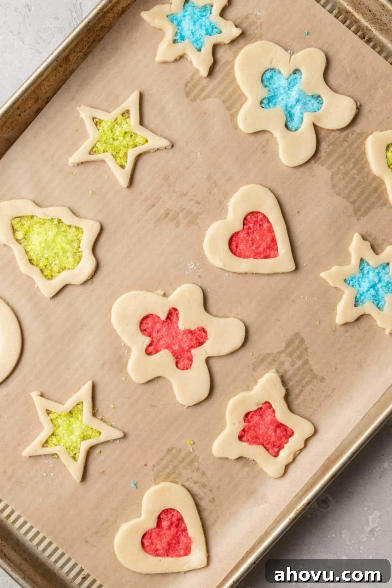 An overhead view of unbaked stained glass cookies with crushed candy in their centers, arranged on a baking sheet lined with parchment paper.