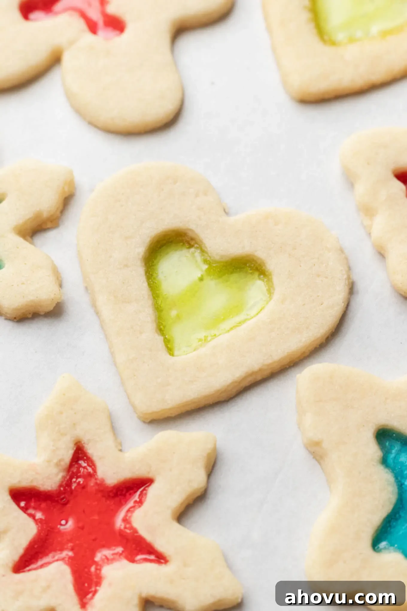 An close-up, overhead view of freshly baked stained glass window cookies cooling on parchment paper, showcasing their glossy, colorful centers.