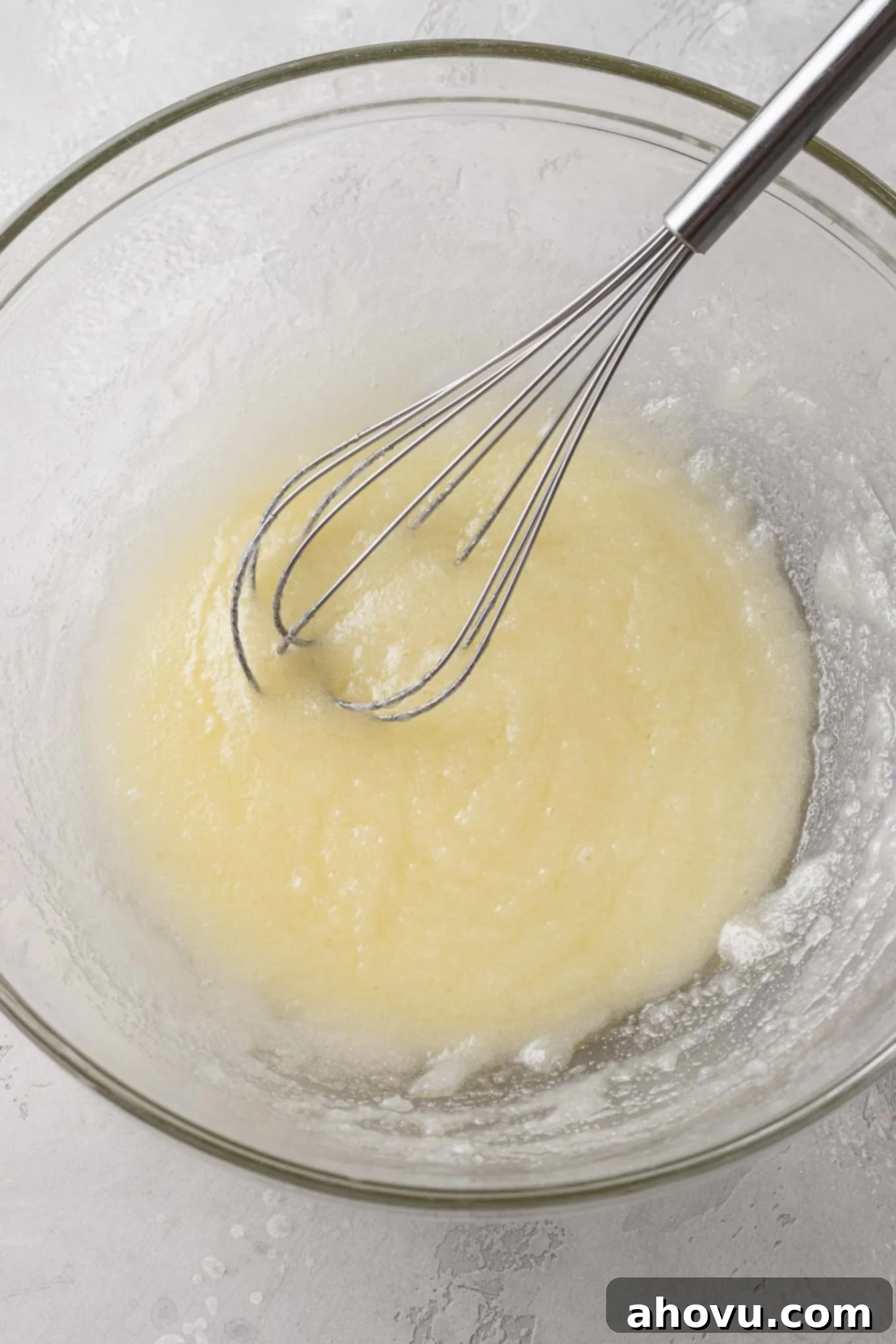 An overhead view of melted butter and sugar in a glass mixing bowl with a whisk. 