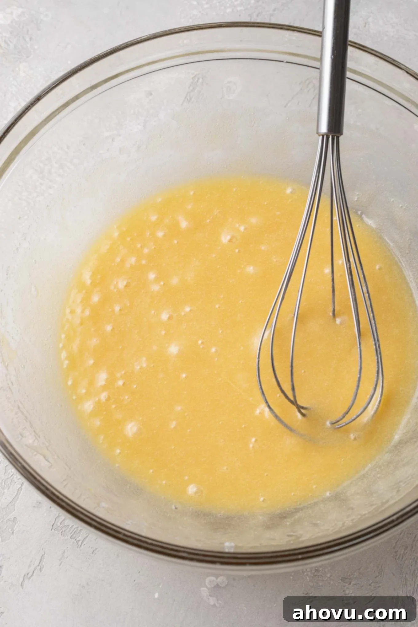 An overhead view of melted butter, eggs, and sugar in a glass mixing bowl with a whisk. 