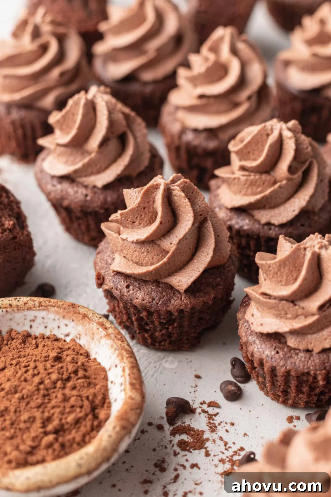 Mini brownies topped with chocolate whipped cream, next to a bowl of cocoa powder. 