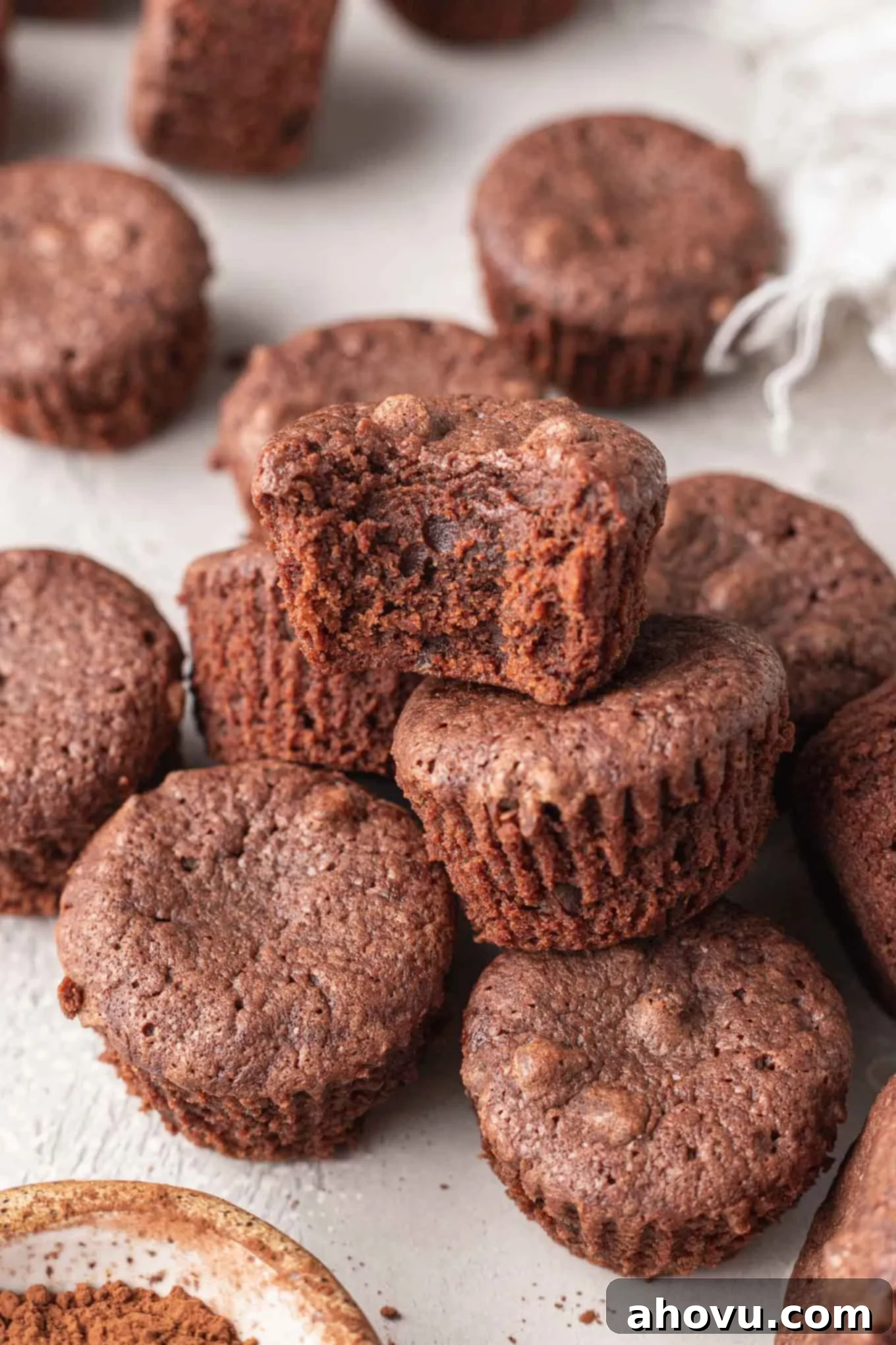 A bite-sized brownie with a bite missing, resting atop a pile of brownies. 