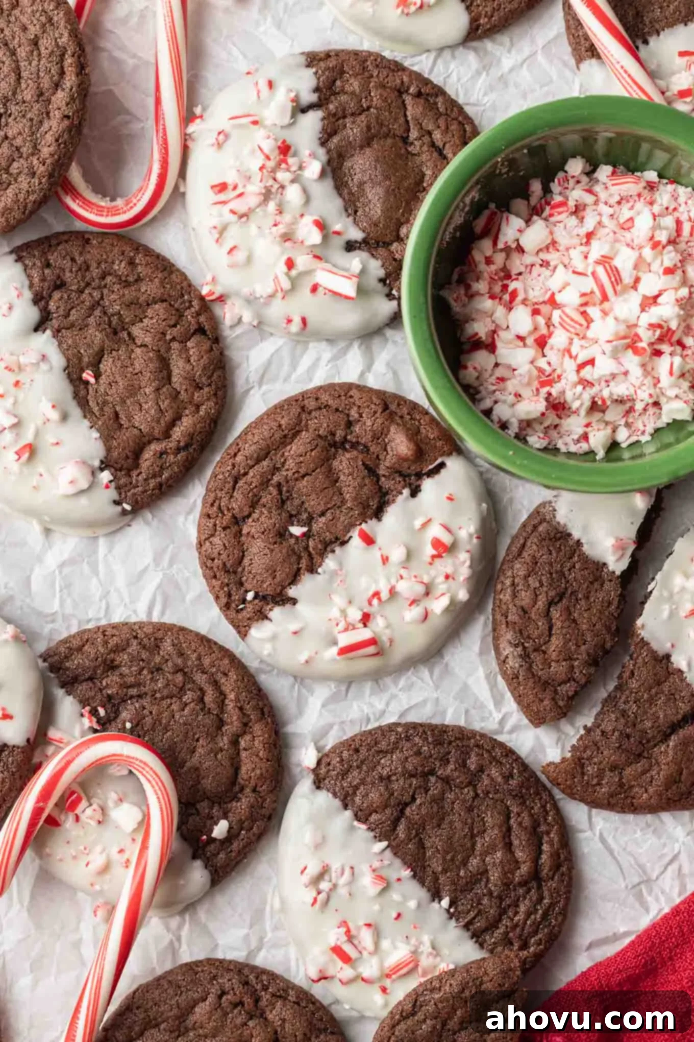 An overhead view of white chocolate-dipped chocolate peppermint cookies, with a dish of crushed candy canes. 