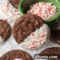 A chocolate cookie coated in white chocolate and crushed candy canes leaning up against a small dish.