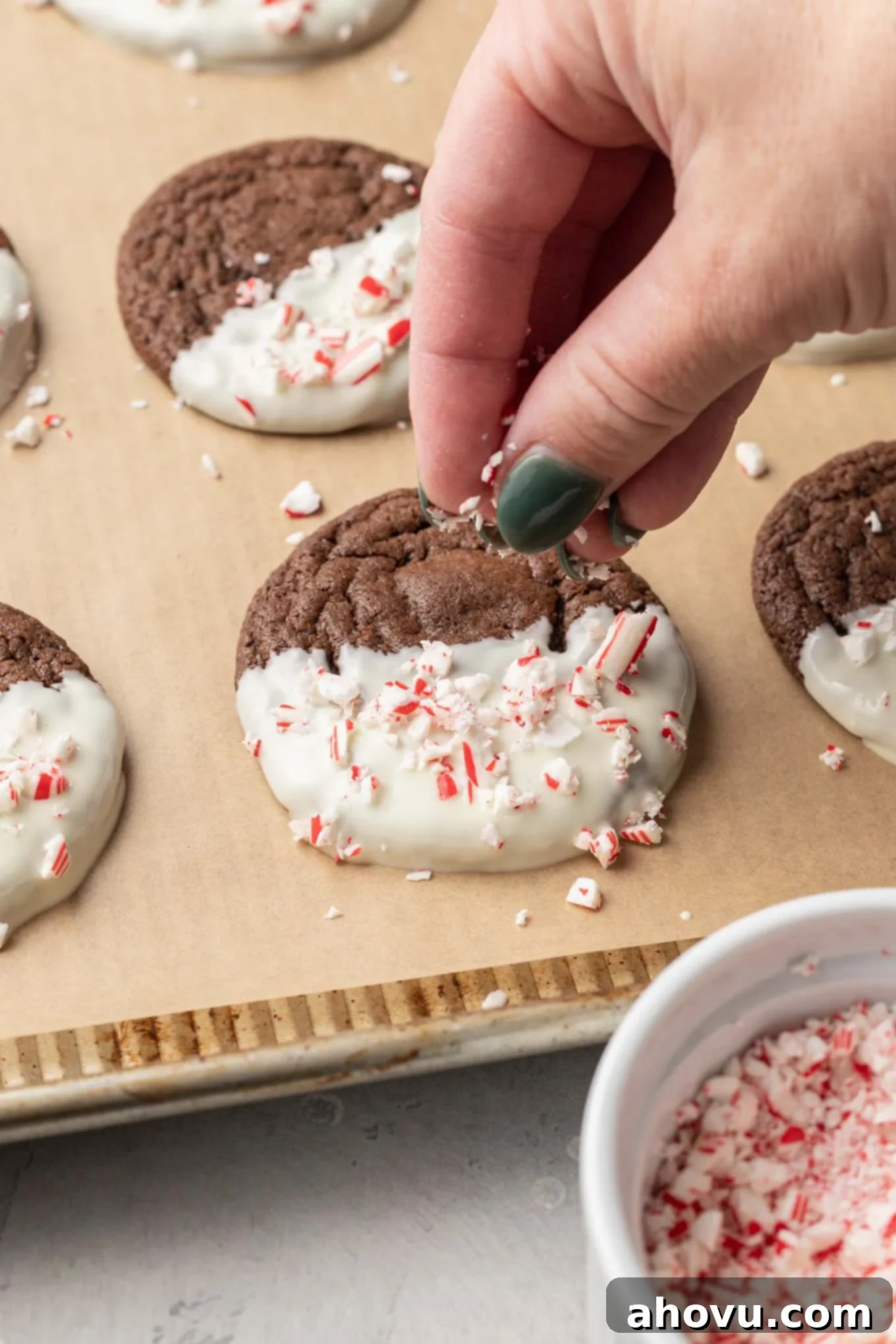 A process shot chowing a chocolate peppermint cookie being topped with crushed candy cane pieces. 