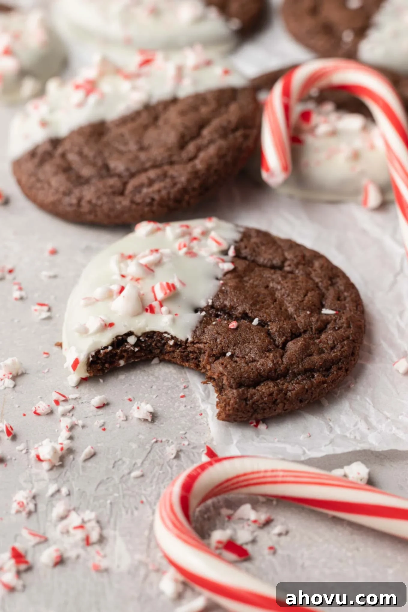 A chocolate peppermint Christmas cookie with a bite missing, surrounded by additional cookies. 