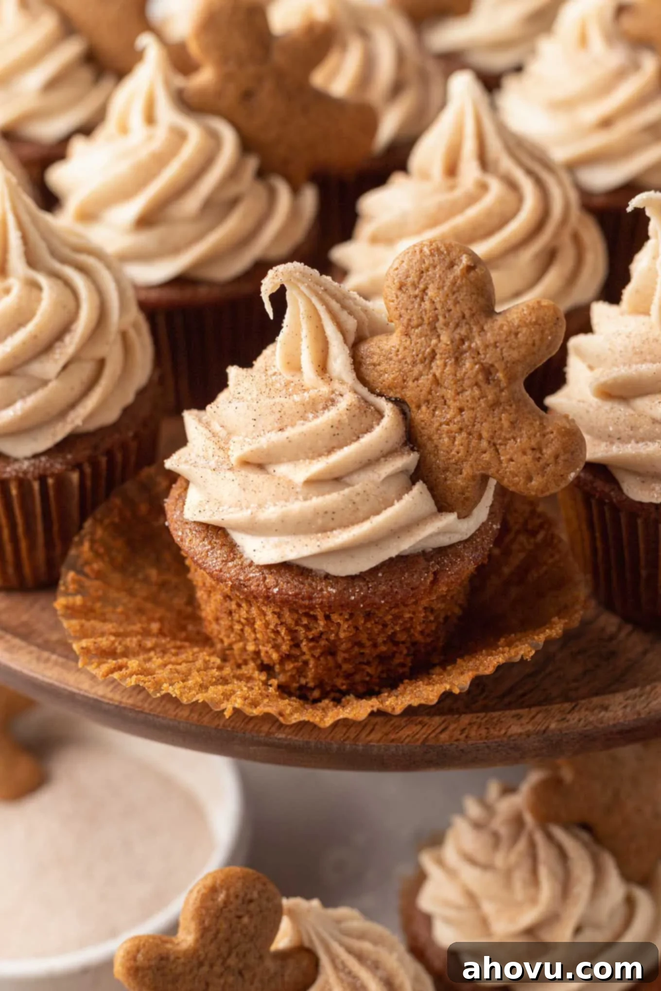 A gingerbread cupcake with the cupcake liner pulled down. More cupcakes are behind it on a cake stand. 