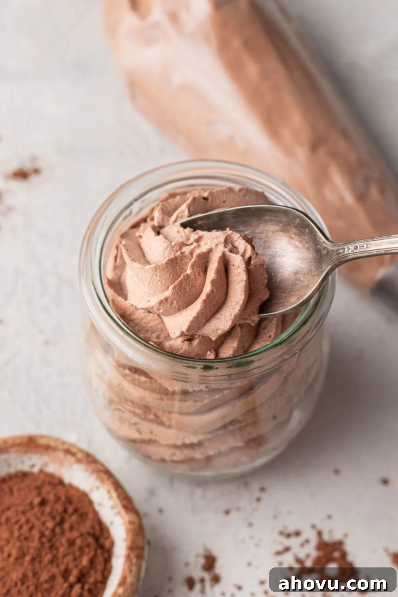 A small jar filled with chocolate whipped cream. A spoon is taking a small scoop out of the whipped cream.