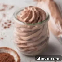 A small jar filled with chocolate whipped cream. A piping bag filled with whipped cream and a small bowl of cocoa powder rest nearby.