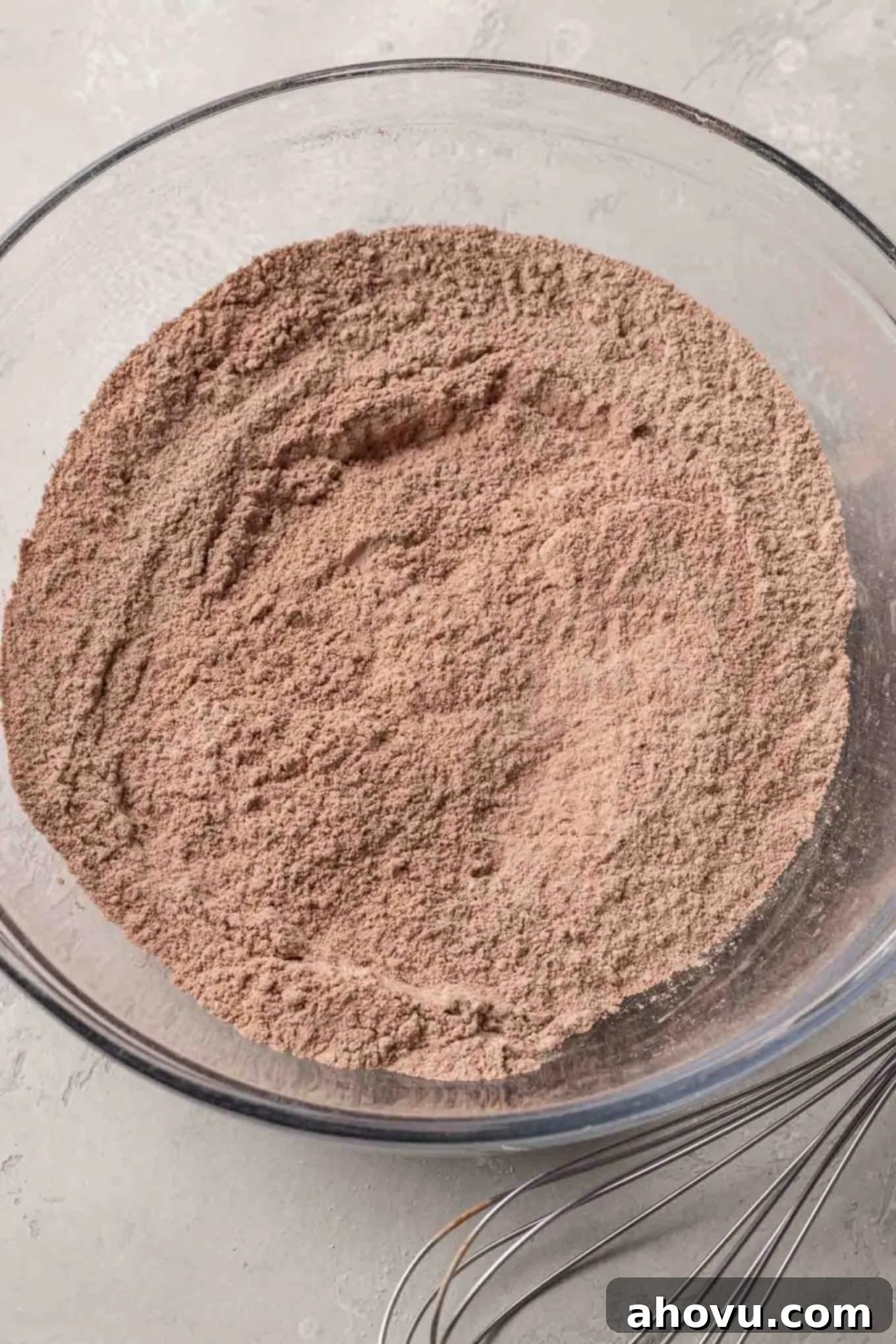 An overhead view of flour and cocoa powder in a glass mixing bowl. 