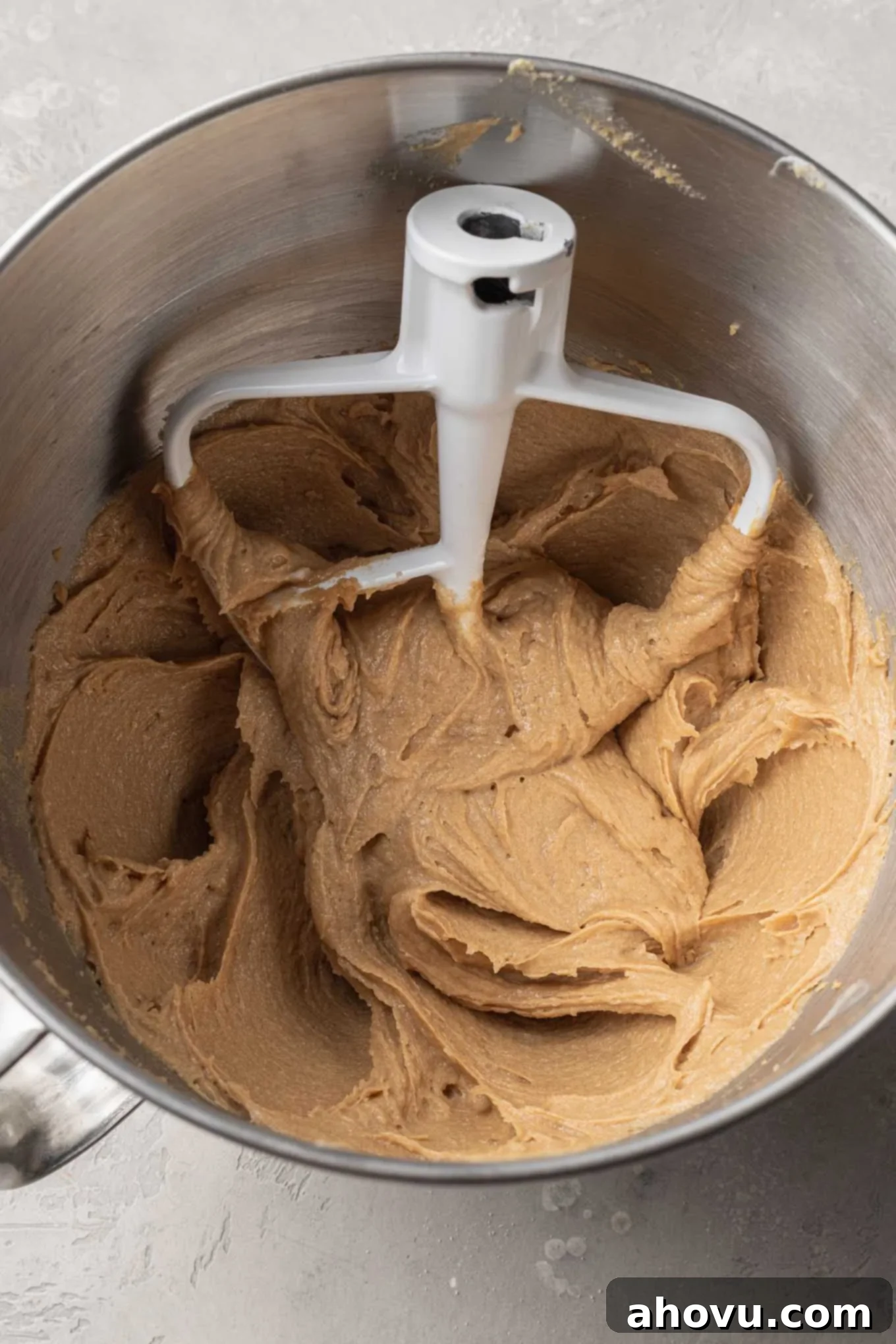 An overhead view of a peanut butter mixture in the bowl of a stand mixer, with a paddle attachment. 