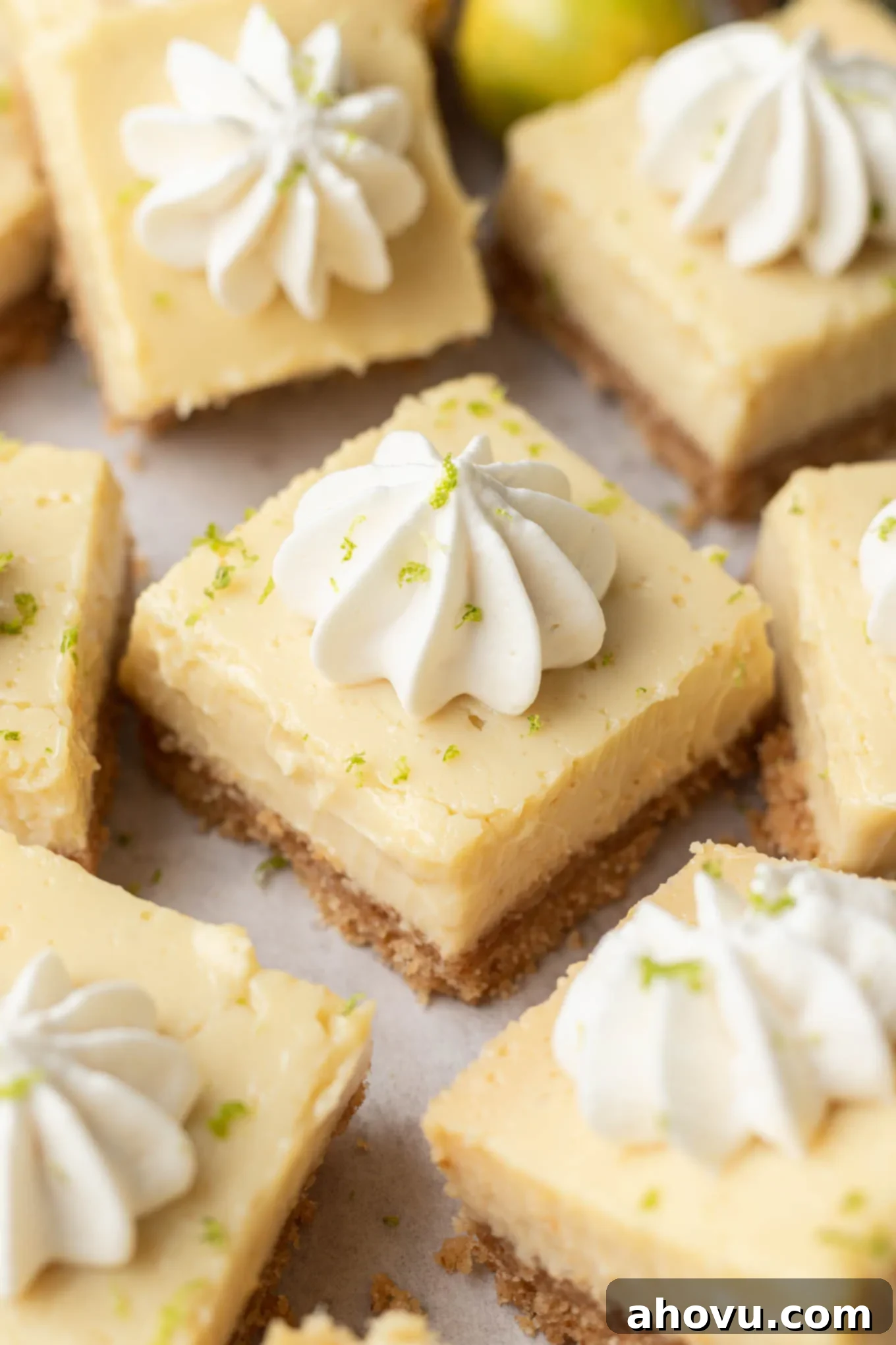 Sliced key lime pie bars garnished with lime zest and dollops of whipped cream. 