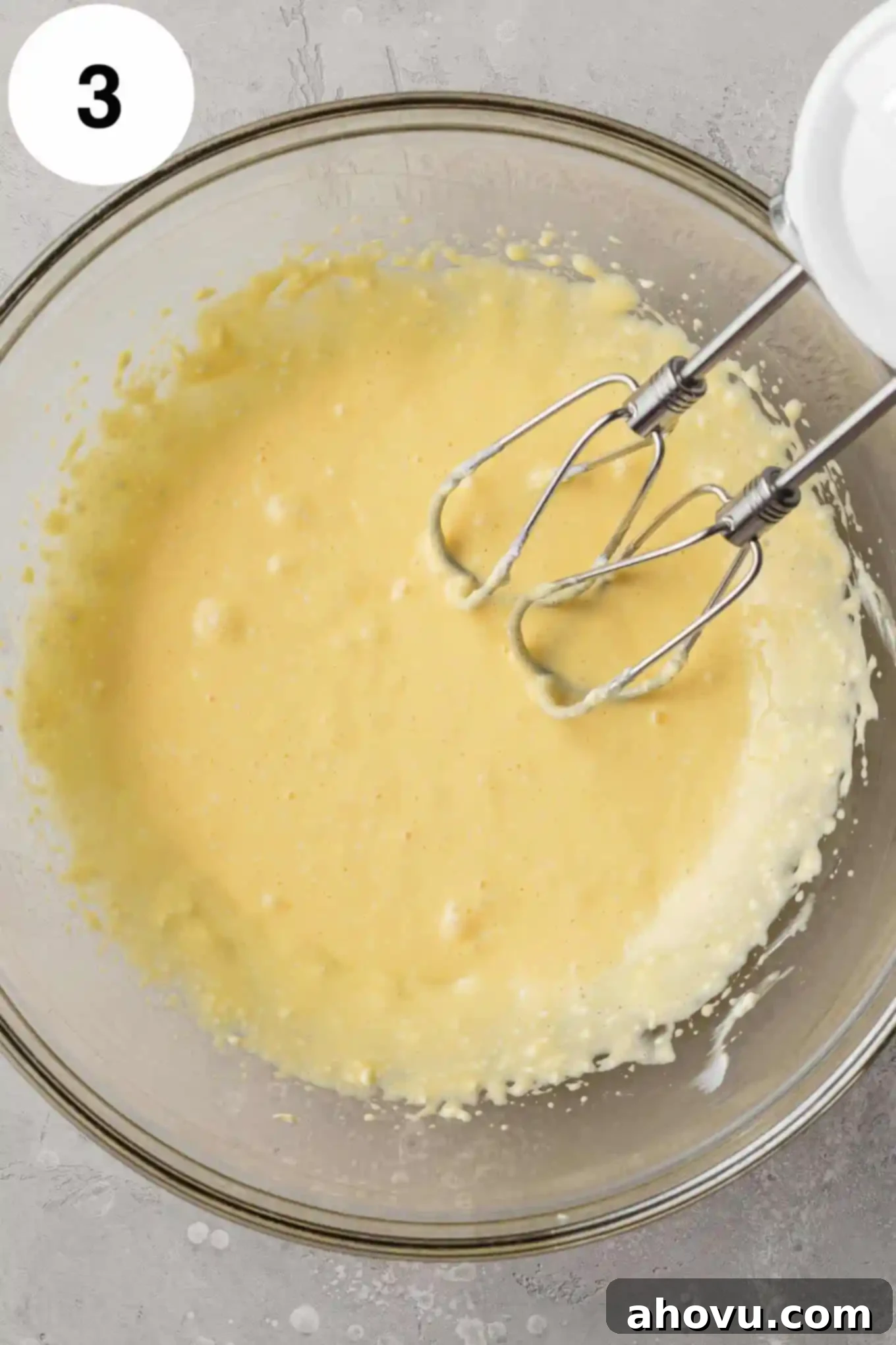 An overhead view of a cream cheese-egg mixture in a glass mixing bowl. 