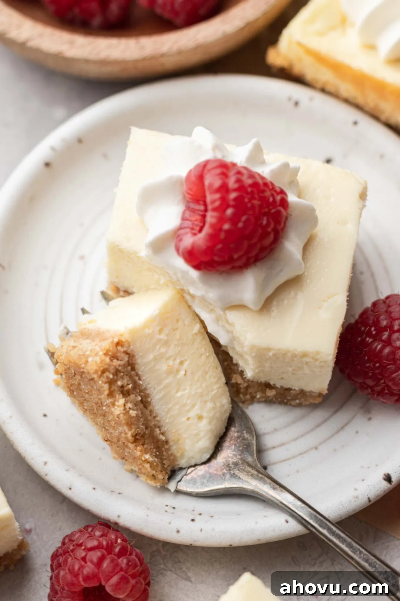 Creamy Cheesecake Squares 11 A close-up view of a cheesecake bar on a dessert plate. A piece has been carved off with a fork and rests on the plate.
