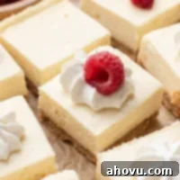 Creamy Cheesecake Squares 13 Several sliced cheesecake bars on a piece of parchment paper. Some of the bars are topped with whipped cream and a raspberry.